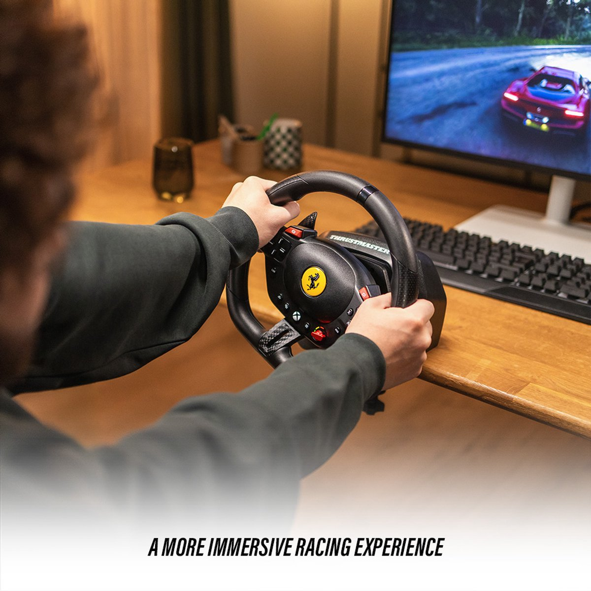 Una persona sostiene un volante de carreras, jugando un juego de carreras en un monitor. El volante tiene un logo de Ferrari. Un teclado es visible.