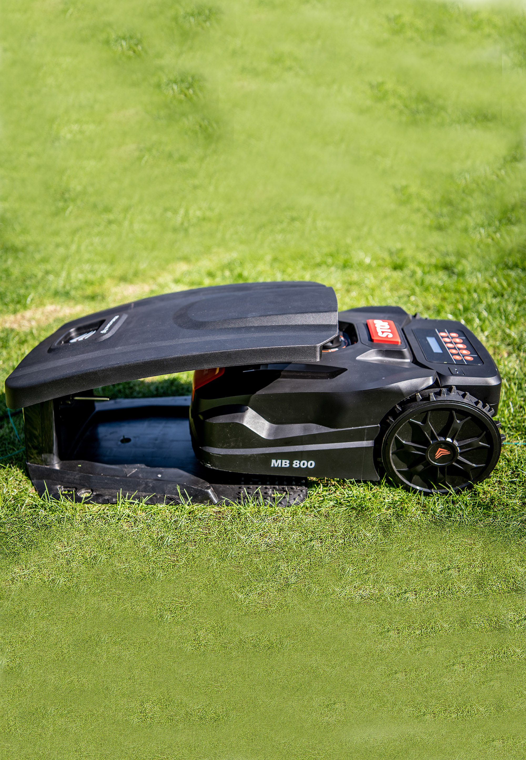 Ein schwarzer Roboter-Rasenmäher auf grünem Gras. Er hat einen hochgeklappten Deckel und den Text MB 800.