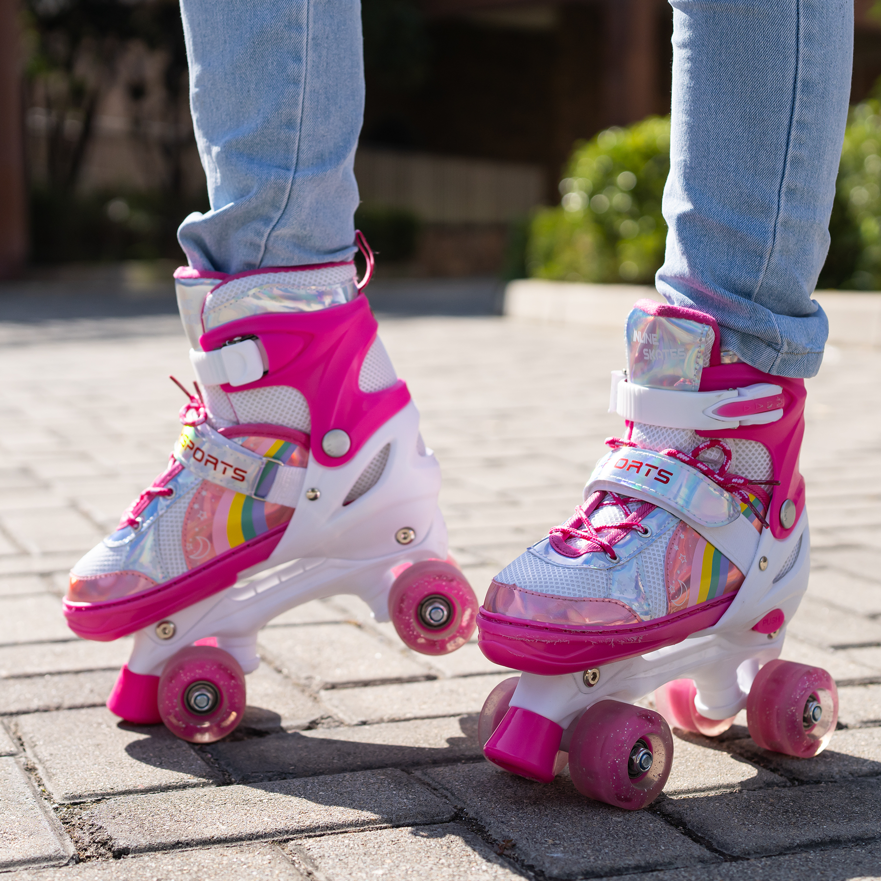 Person trägt pinke und weiße Rollschuhe mit Regenbogenakzenten und pinken Rädern auf einer Ziegeloberfläche.
