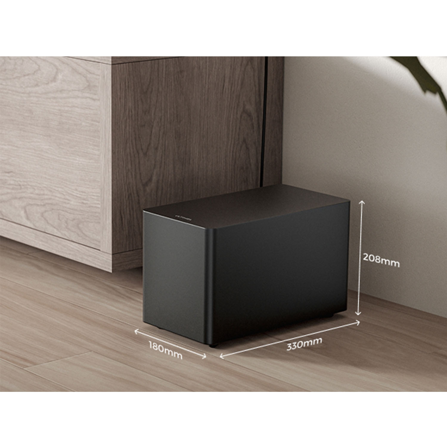 Czarny, prostokątny subwoofer na drewnianej podłodze, z wymiarami. Po lewej stronie drewniana szafka, z tyłu ściana.