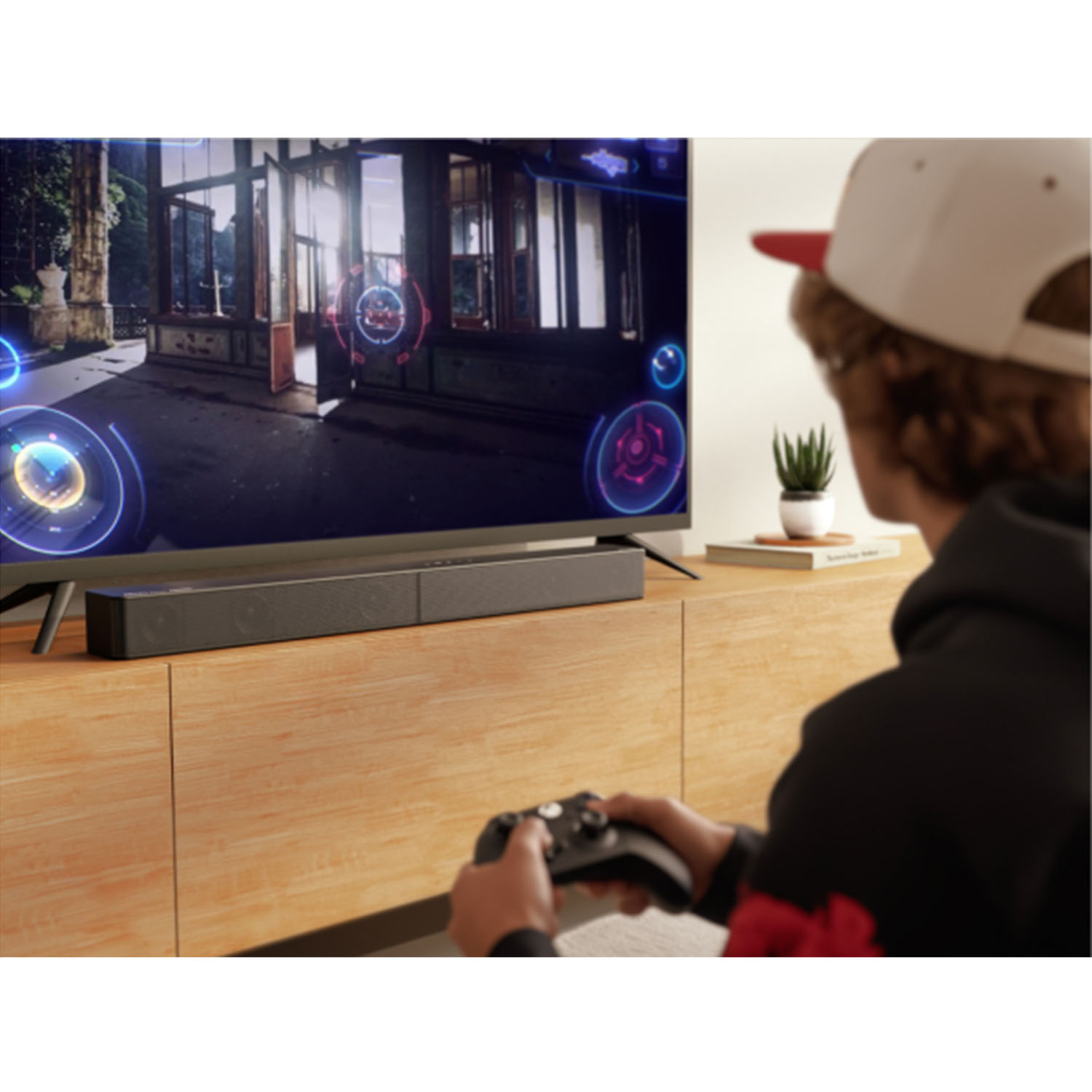 Osoba grająca w grę wideo w telewizji. Ekran pokazuje scenę z gry. Soundbar pod telewizorem, kontroler w dłoniach.