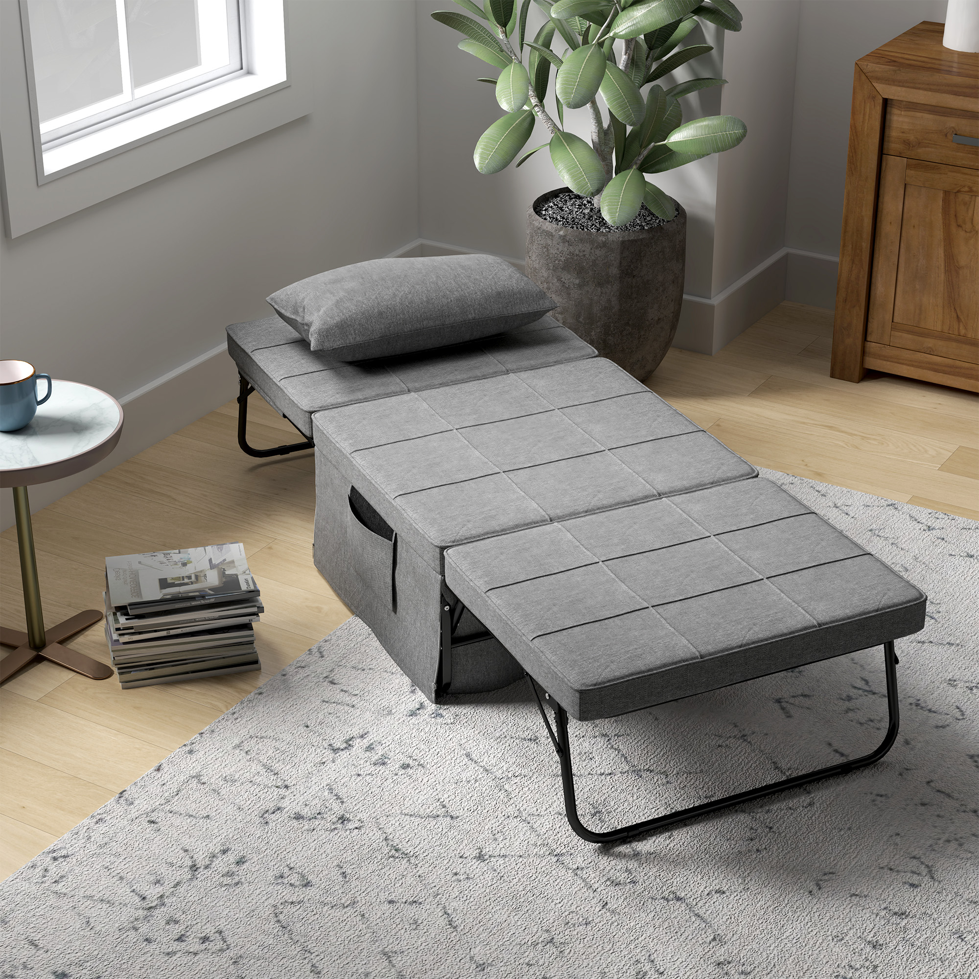 Un divano letto grigio convertibile è aperto in una stanza. Un cuscino poggia sulla testa. Una pianta e un armadio sono sullo sfondo.