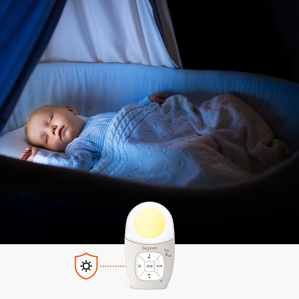 Een baby slaapt in een wieg, bedekt met een deken. Een babyfoon met een lampje staat op de voorgrond. De scène is donker.