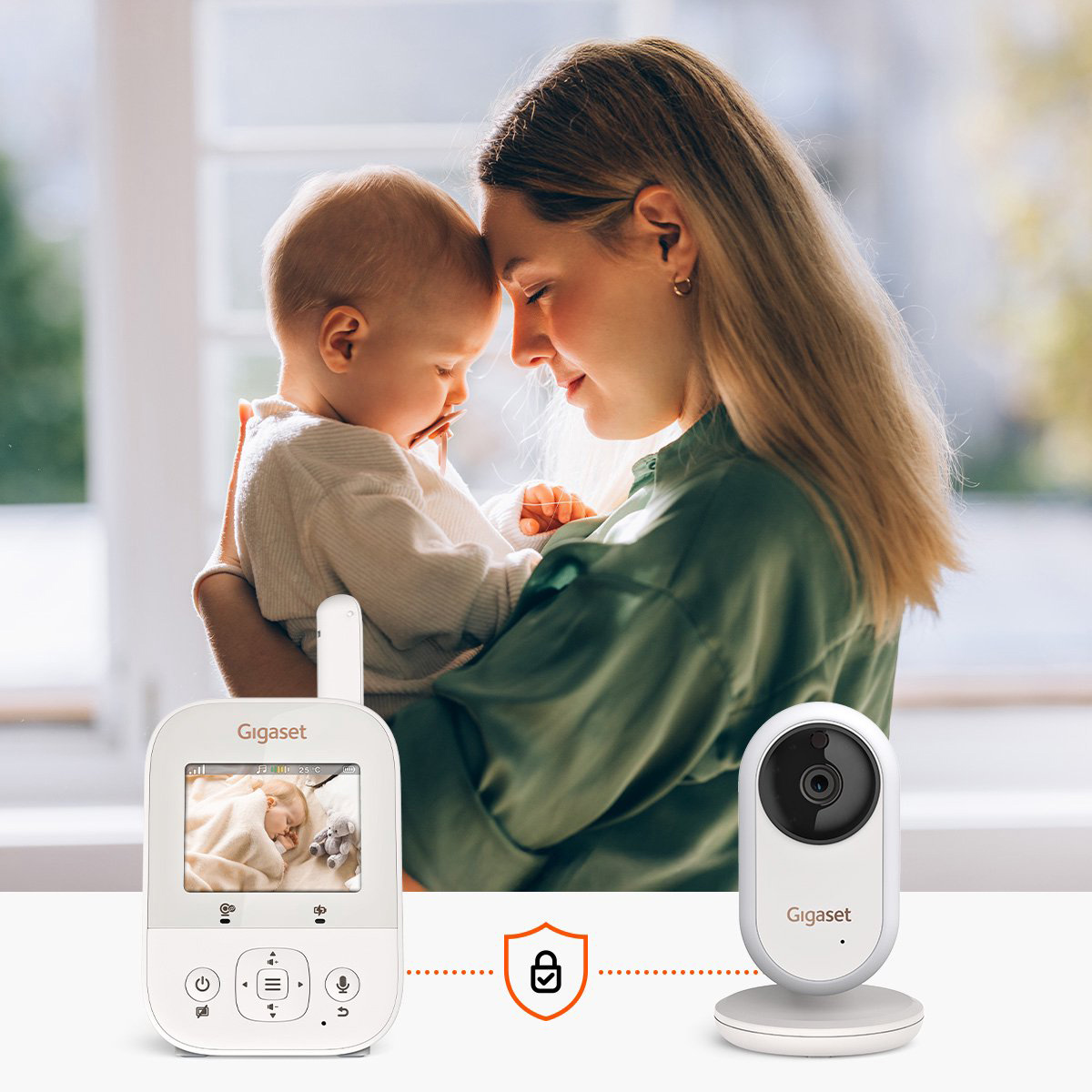 Una madre tiene in braccio un bambino. Un baby monitor e una telecamera sono in primo piano. Il monitor mostra un bambino che dorme.