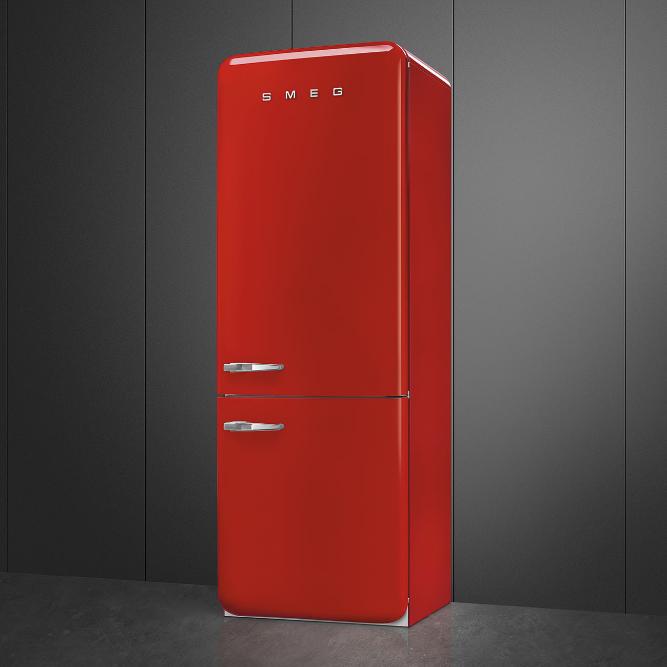 Un refrigerador rojo SMEG se encuentra contra una pared de paneles gris oscuro. El refrigerador tiene dos puertas y manijas cromadas. El piso es gris.