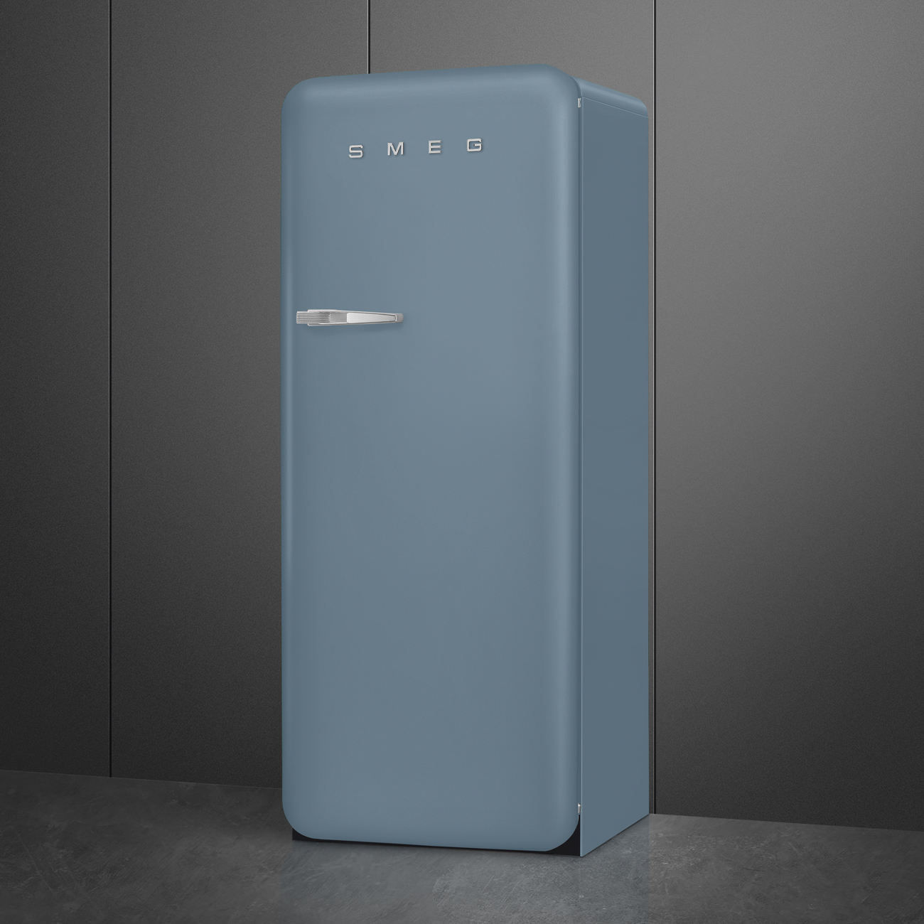 Ein blauer Smeg-Kühlschrank steht vor einer dunkelgrauen Wand. Der Kühlschrank hat einen silbernen Griff und den Markennamen oben.