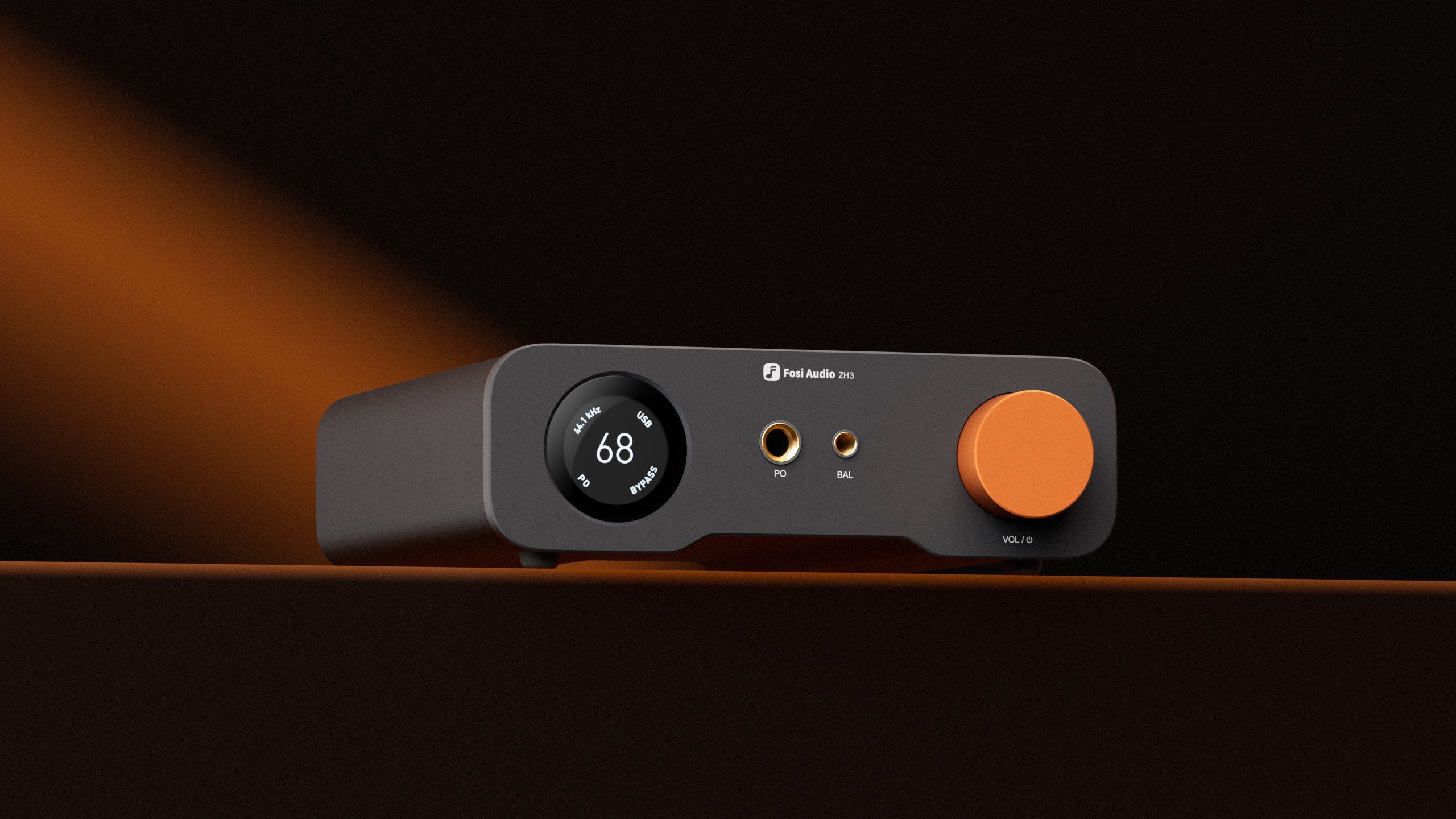 Un dispositivo de audio gris oscuro con una perilla y pantalla naranja. La pantalla muestra números y texto. El fondo es naranja oscuro.