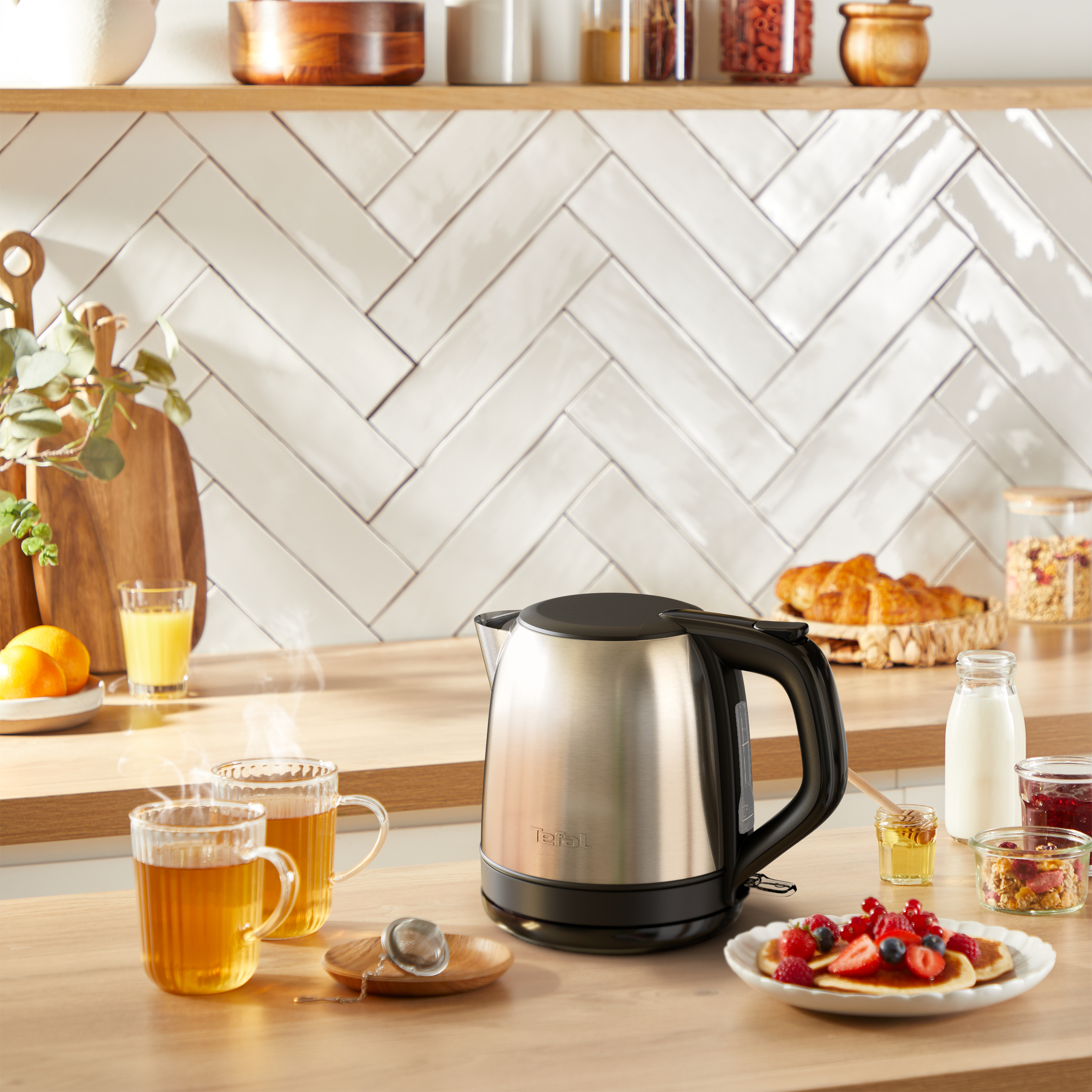 Eine Küchenszene mit Wasserkocher, Tee, Pfannkuchen und Frühstückszutaten. Eine warme und einladende Morgenkulisse.