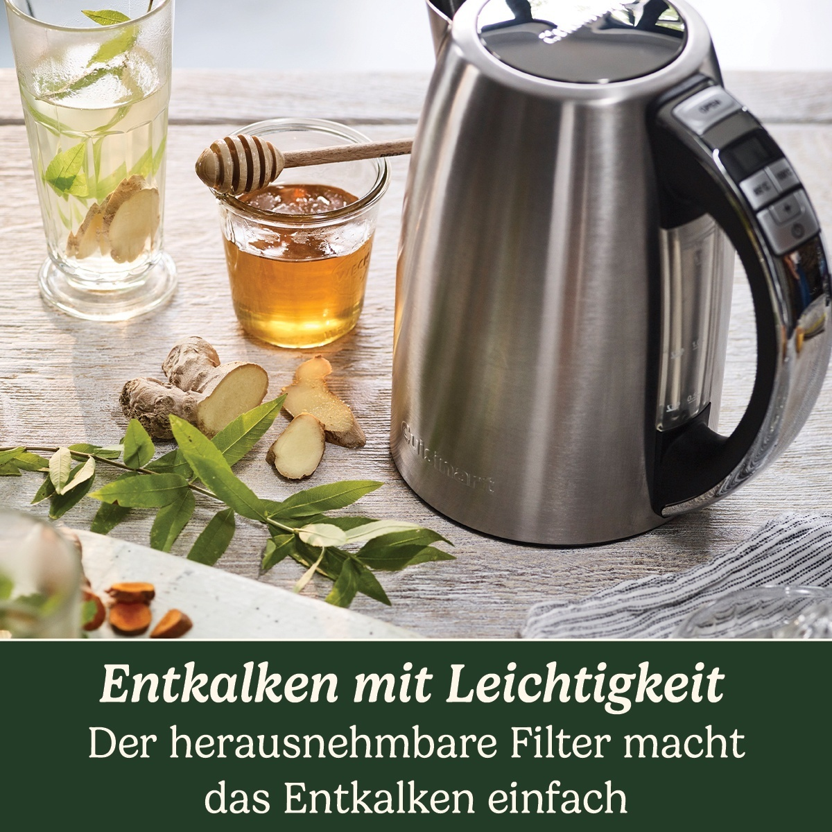 Edelstahl-Wasserkocher, Glas Tee mit Ingwer, Honig und Zutaten liegen auf einem Holztisch. Text unten.