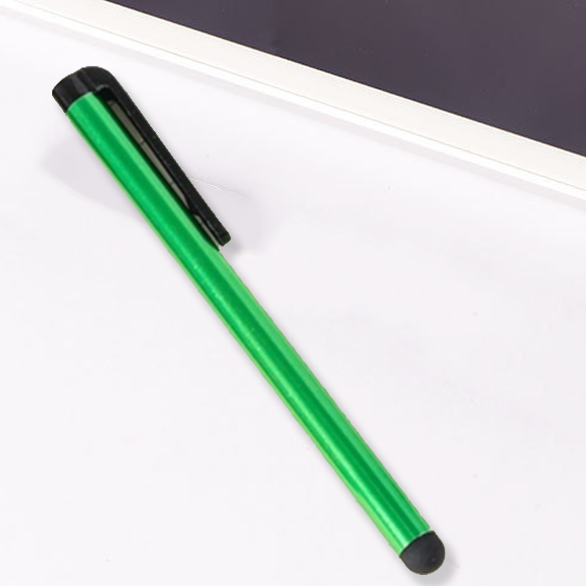 Ein grüner Stift mit schwarzer Kappe liegt diagonal auf einer weißen Oberfläche in der Nähe eines Tablets. Der Stift hat eine schwarze Spitze.