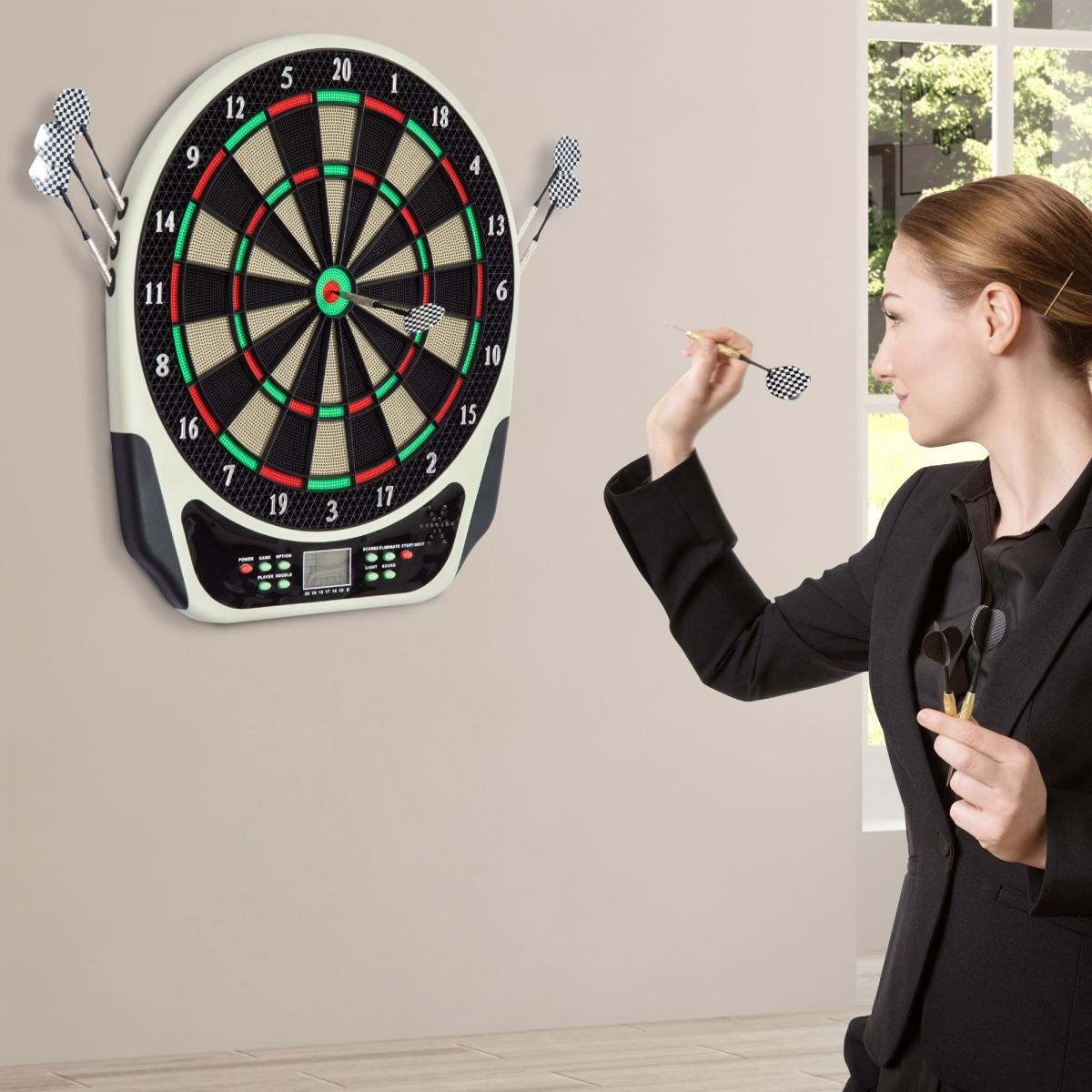 Eine Frau wirft einen Dart auf eine Dartscheibe. Das Board ist an einer Wand befestigt. Sie hat mehrere Darts in der anderen Hand.