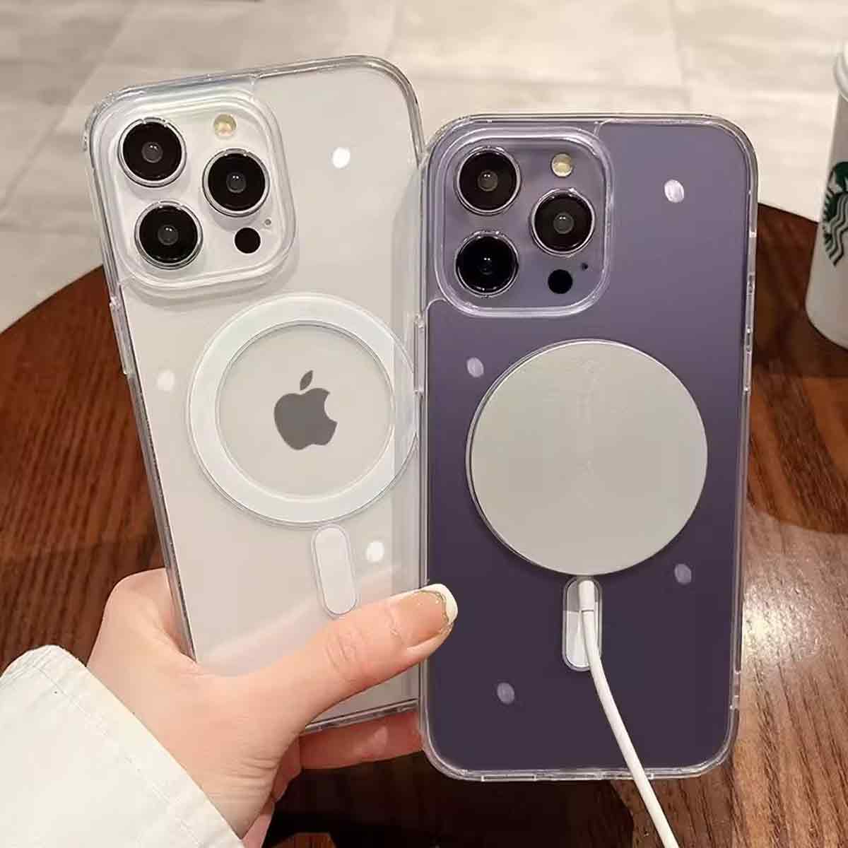 Zwei iPhone-Hüllen, eine durchsichtige und eine lila, werden von einer Hand gehalten. Beide haben magnetische Ladegeräte. Ein Starbucks-Becher ist im Hintergrund.