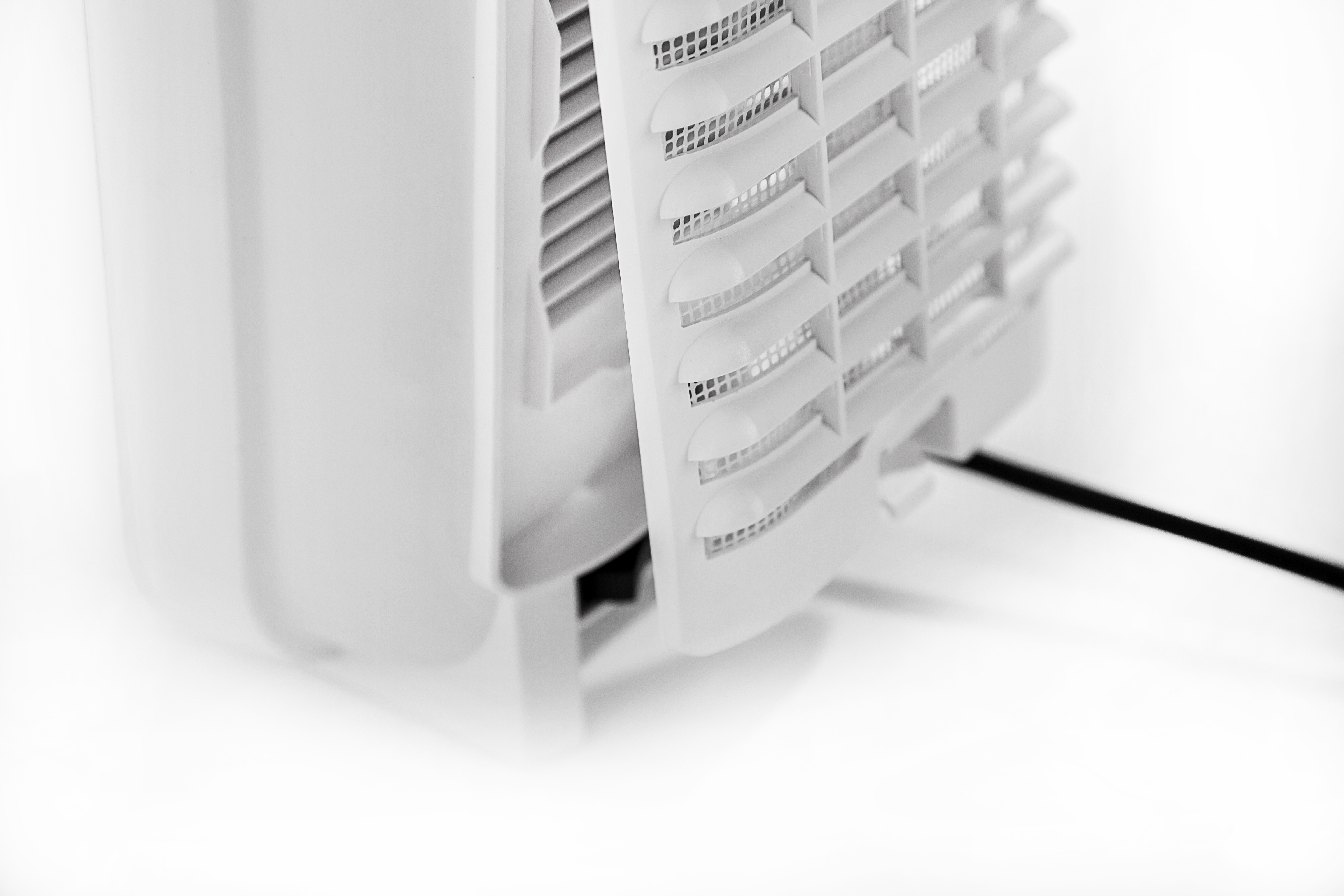 Primo piano di un purificatore d'aria bianco. Visibili il pannello frontale a lamelle, il lato e un cavo nero.