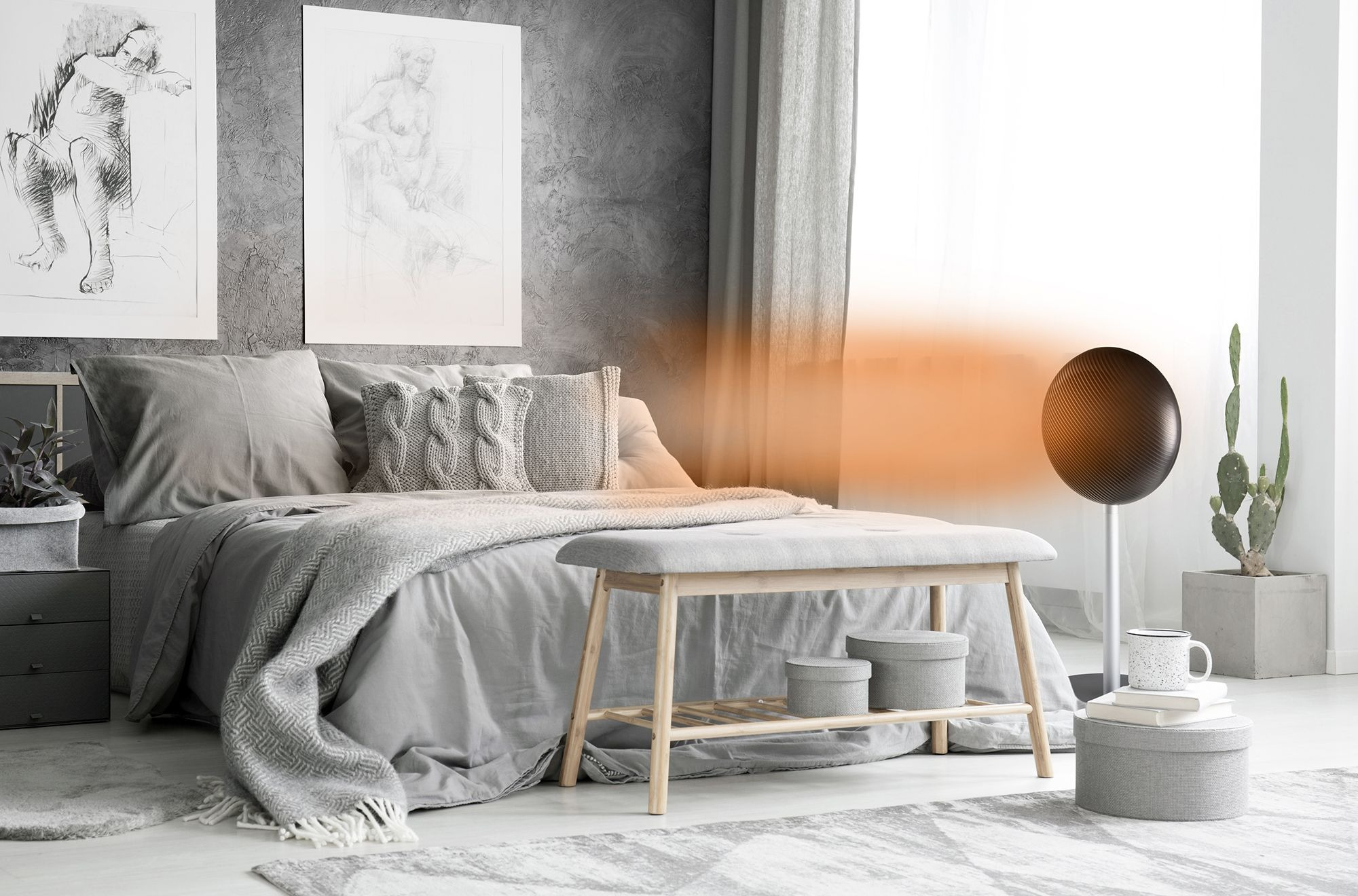 Schlafzimmer mit grauem Bett und Bank, Kunst und einem runden Lautsprecher. Rechts eine Kaktee im Topf.