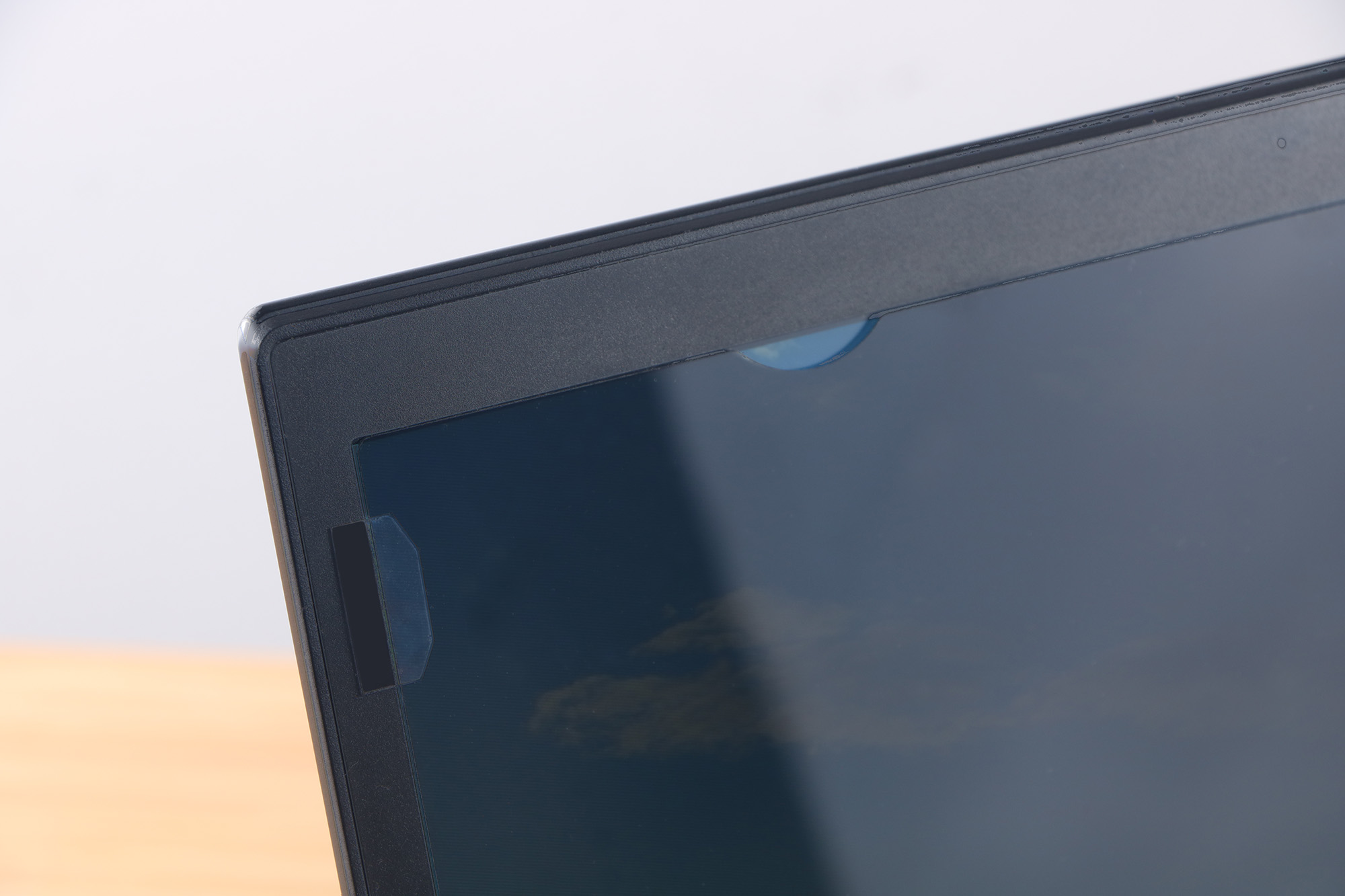 Zbliżenie ekranu i ramki laptopa. Widoczna osłona kamery internetowej. Ekran odbija zachmurzone niebo.