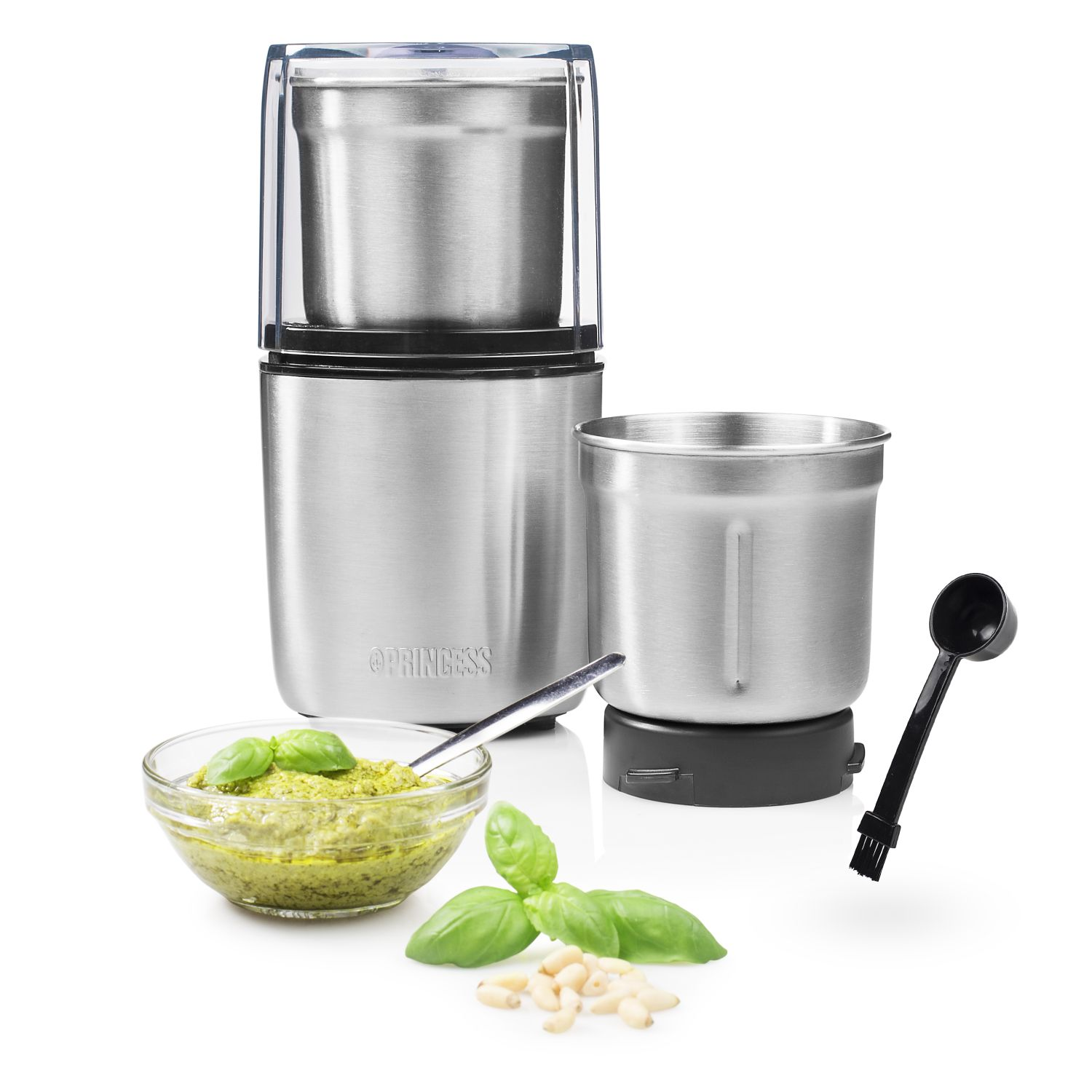 A stainless steel coffee grinder with pesto, basil, and pine nuts. A black spoon with a brush is also present.