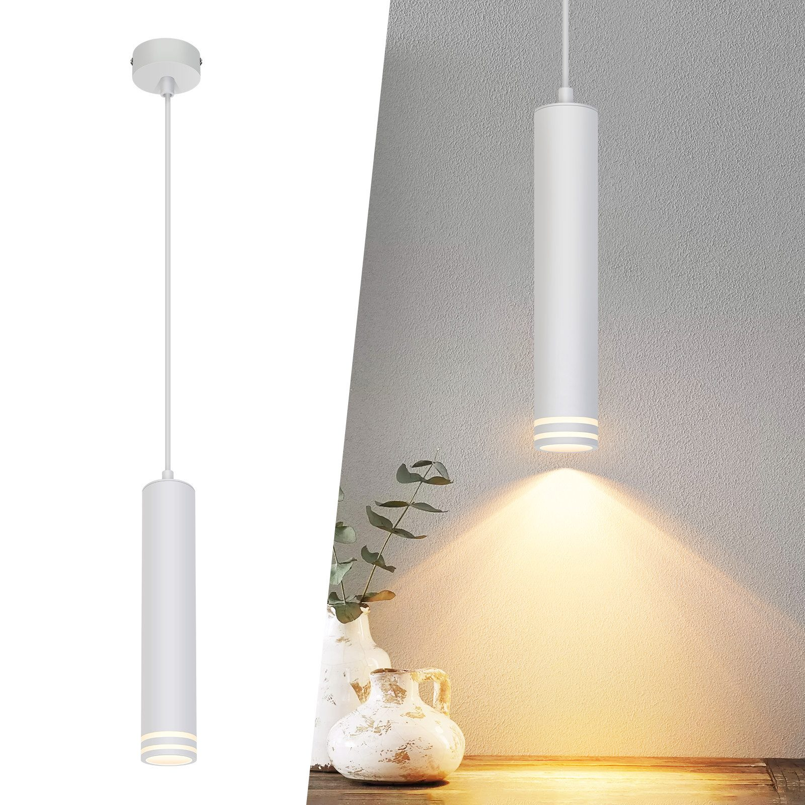 Lampada a sospensione cilindrica bianca. La lampada è appesa. Un fascio di luce è visibile. Un vaso e una pianta sono a destra.