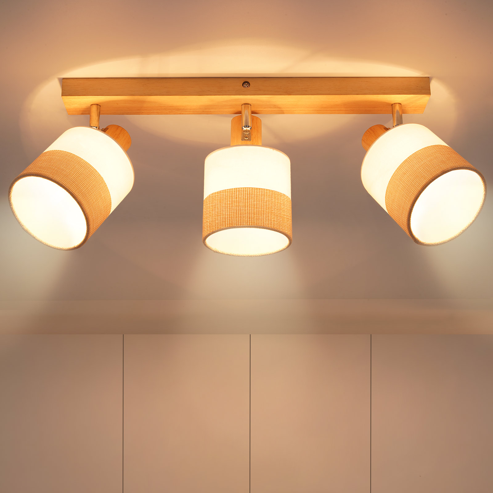 Una plafoniera in legno con tre lampade. Ognuna ha un paralume bianco con una fascia beige. Lo sfondo è un soffitto bianco.