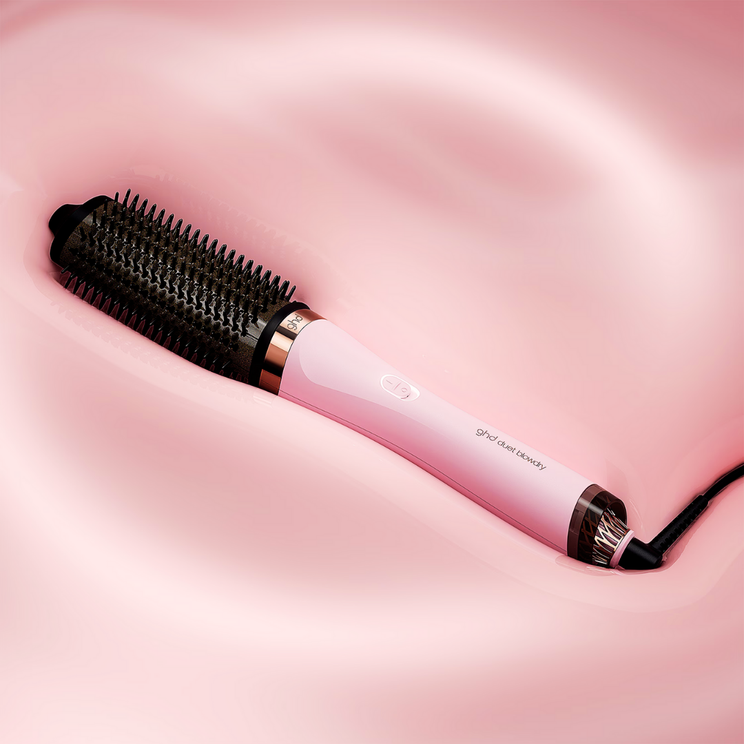 Eine rosa-schwarze ghd Duett-Föhnbürste liegt auf einem rosa Seidenhintergrund. Es hat einen schwarzen Bürstenkopf und einen rosa Griff.