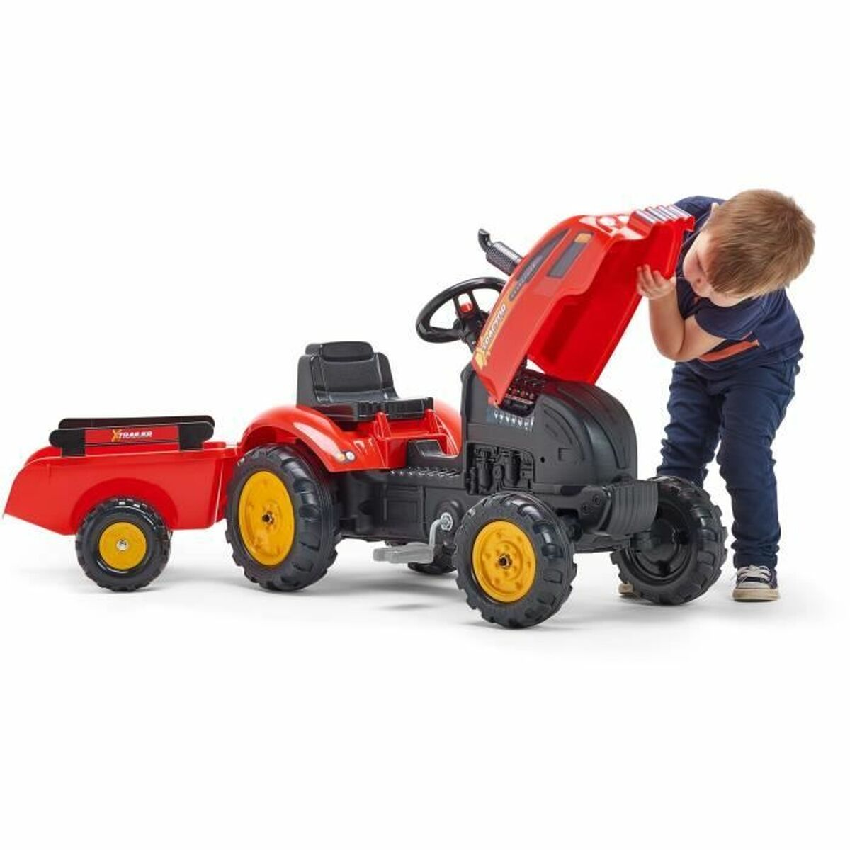 Ein Kind untersucht einen roten Spielzeugtraktor mit Anhänger. Der Traktor hat gelbe Räder, die Haube ist offen. Das Kind trägt Blau.