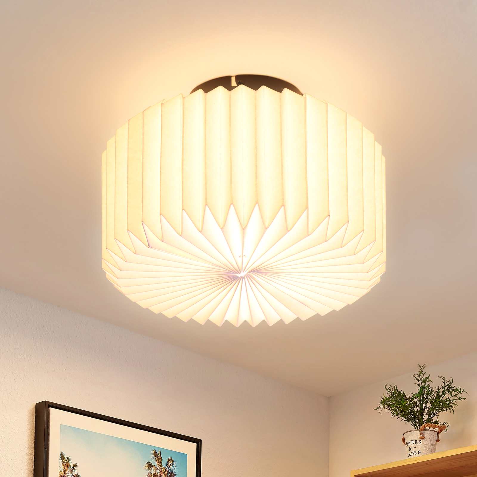 Una moderna lampada da soffitto con un design a carta piegata. Pende dal soffitto, illuminando la stanza con luce soffusa.