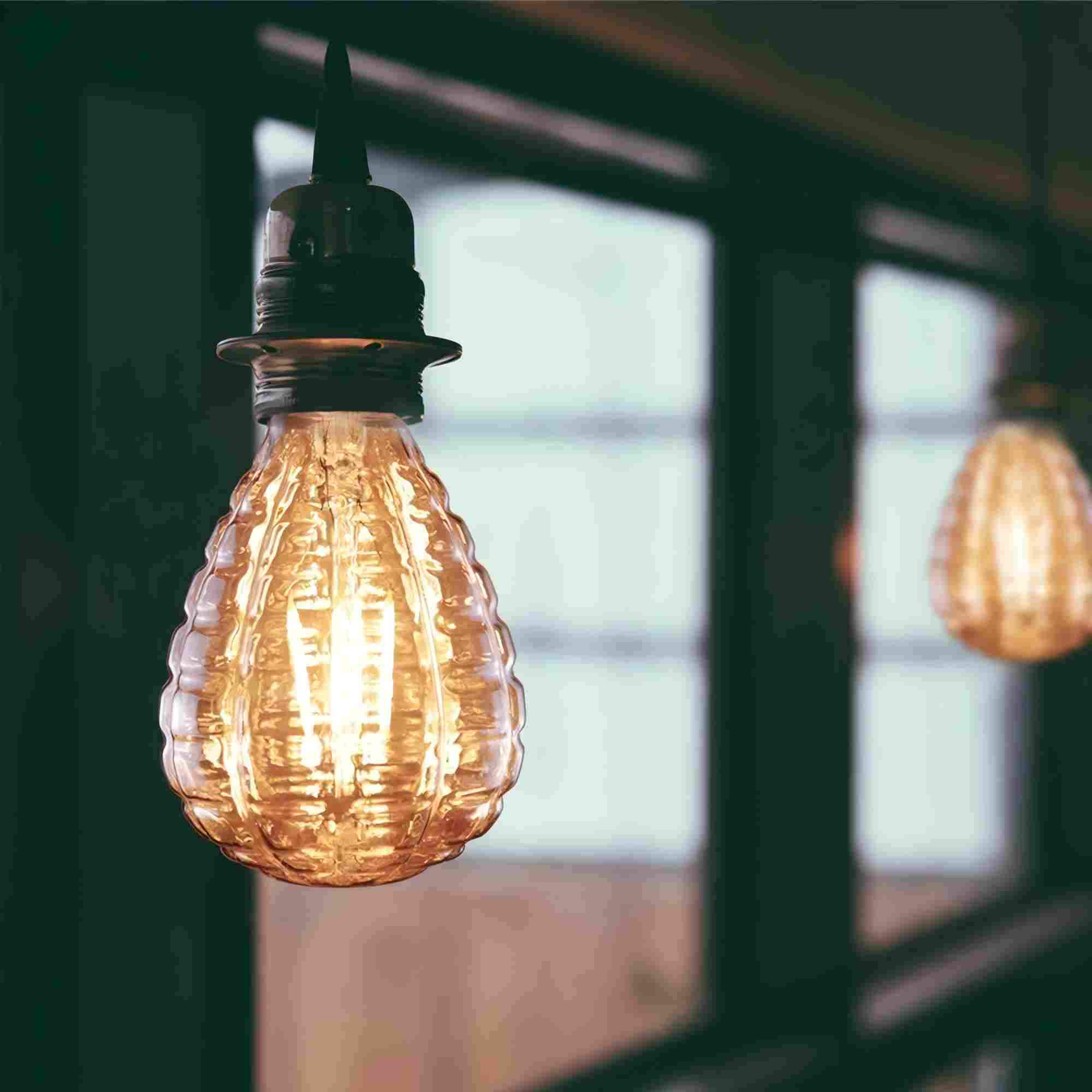 Un primo piano di una lampadina accesa con vetro strutturato. Un'altra lampadina è sfocata sullo sfondo.