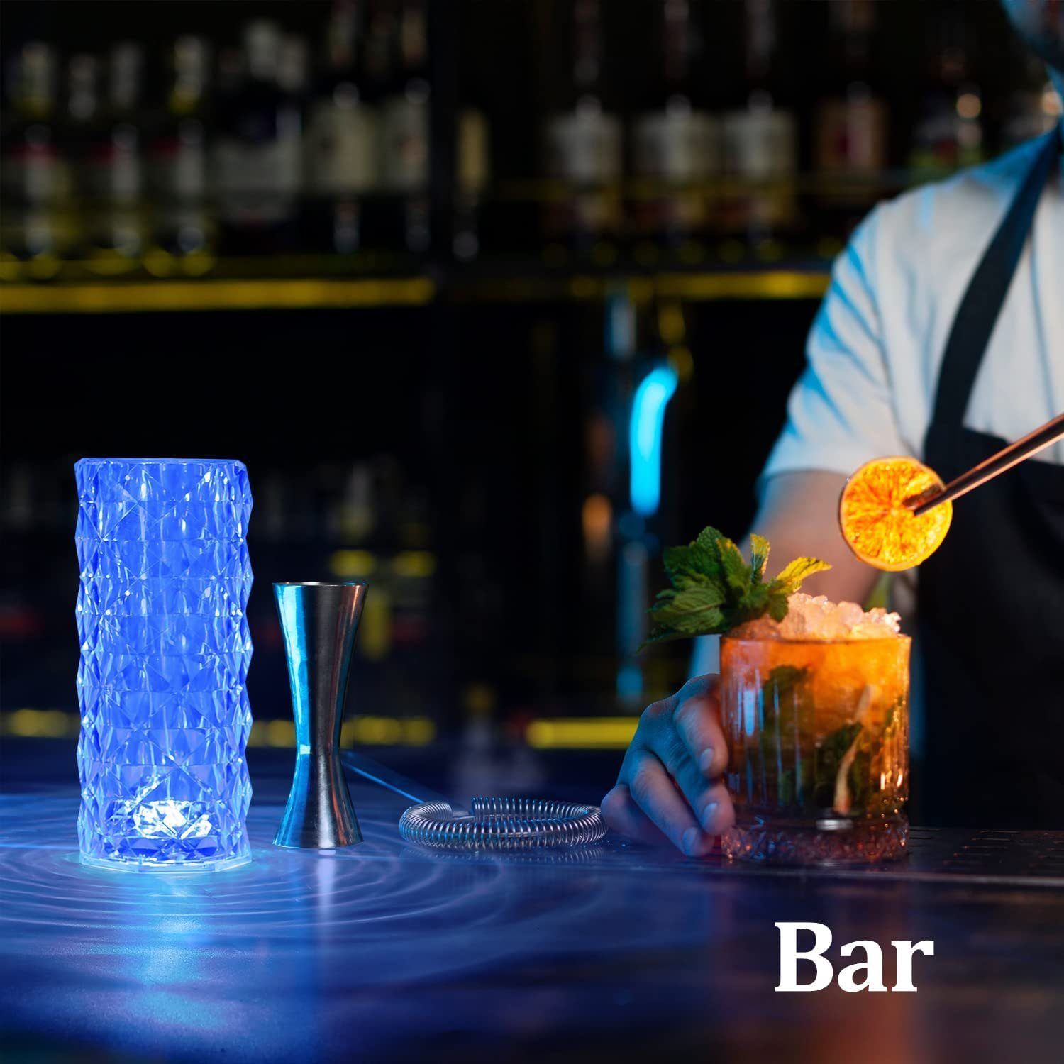 Scena di un bar con un cocktail guarnito con una fetta d'arancia. Una lampada blu e strumenti da bar in primo piano.