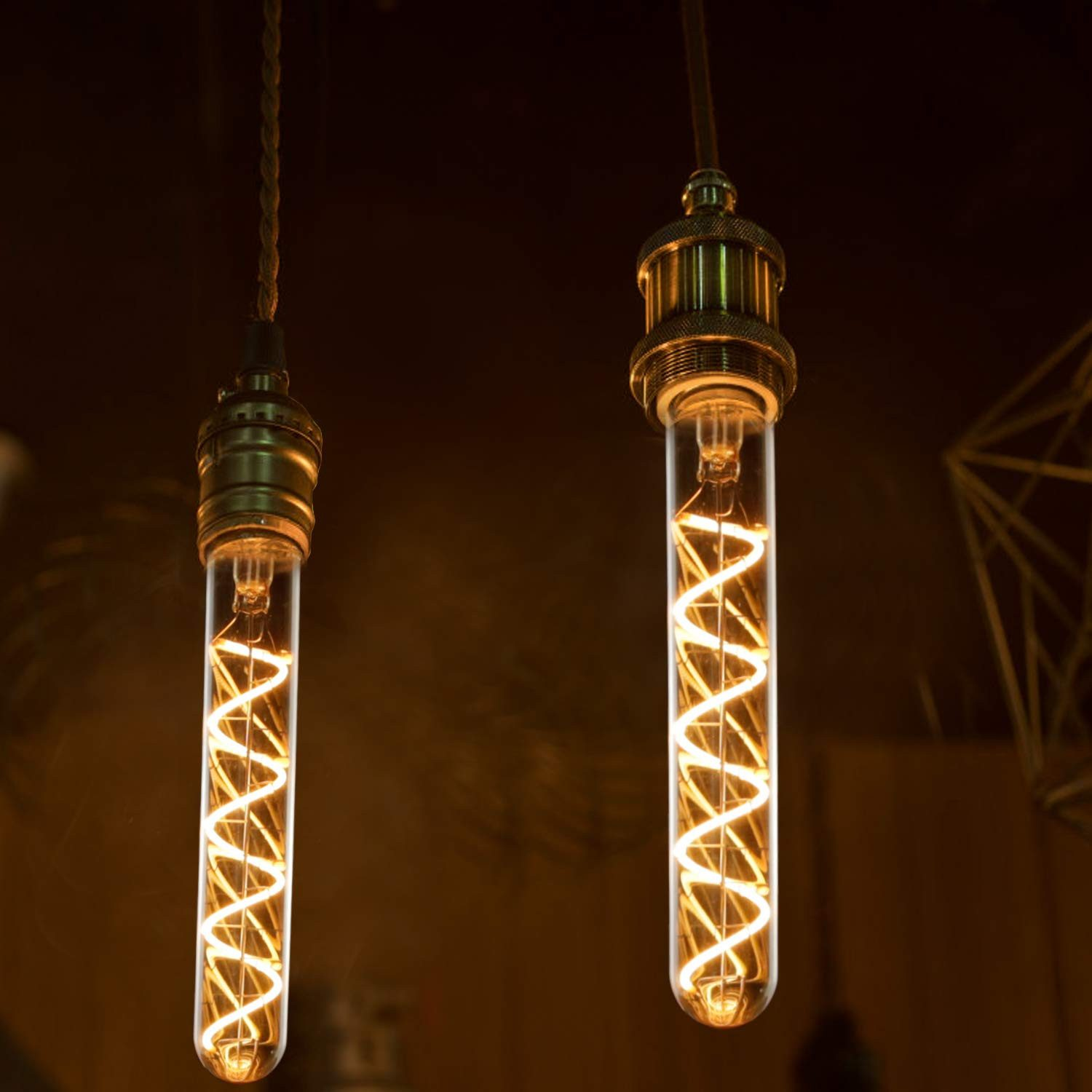 Due lampadine Edison sospese con filamenti a spirale. Sono racchiuse in tubi di vetro, con raccordi in ottone, su sfondo scuro.