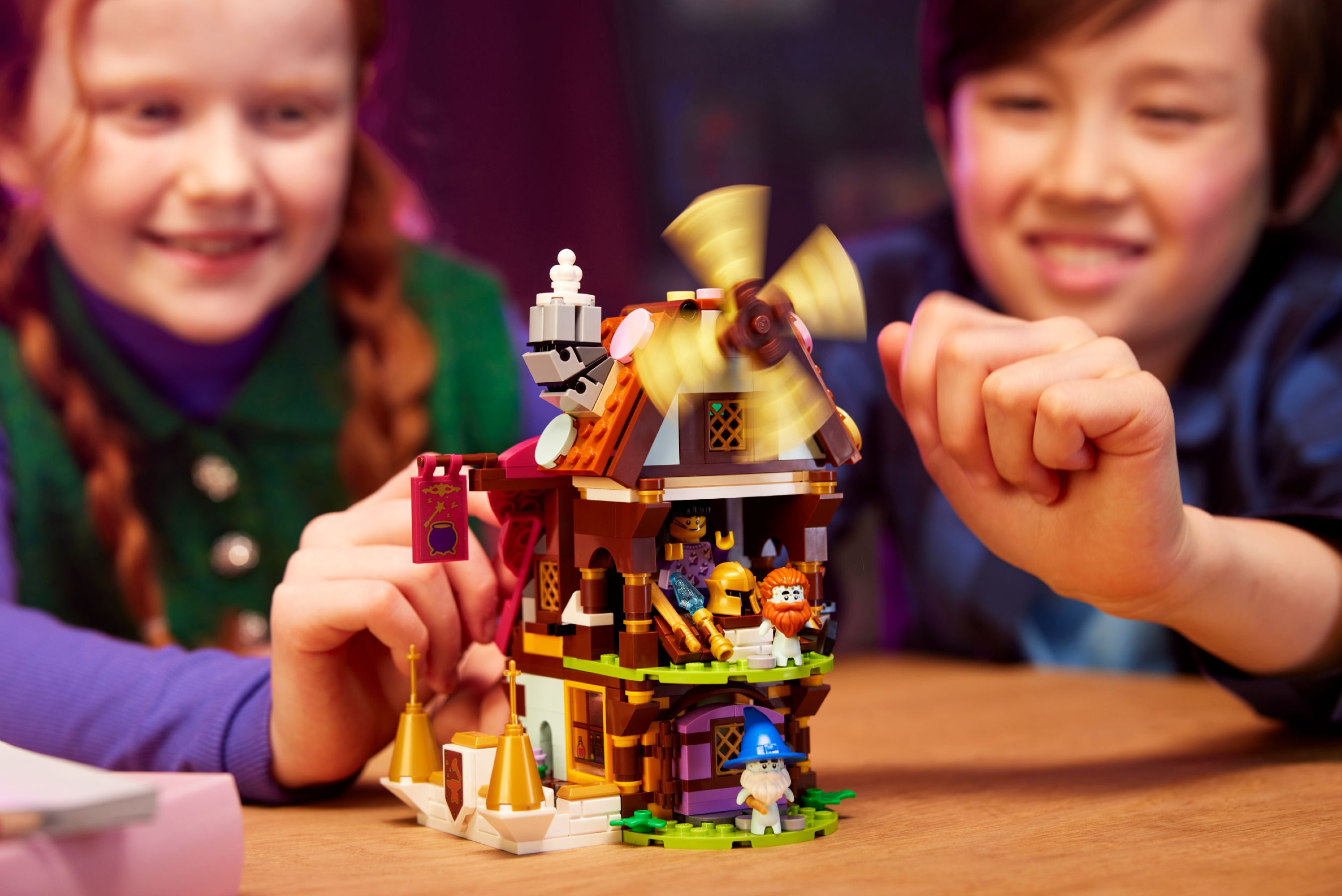 Dwoje dzieci bawi się domkiem z klocków Lego. Domek ma wiatrak i kilka figurek Lego.