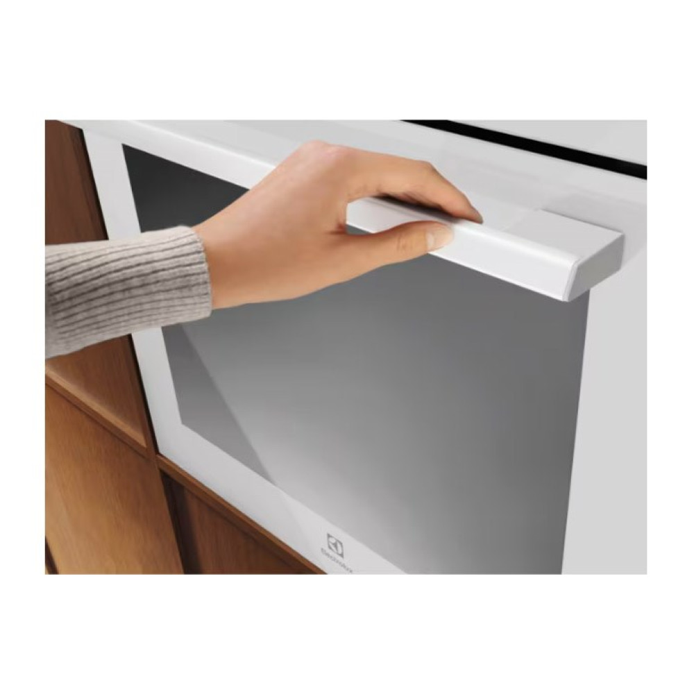Una mano tira la maniglia bianca dello sportello del forno. Lo sportello del forno è bianco con interno grigio. Armadio in legno a sinistra.