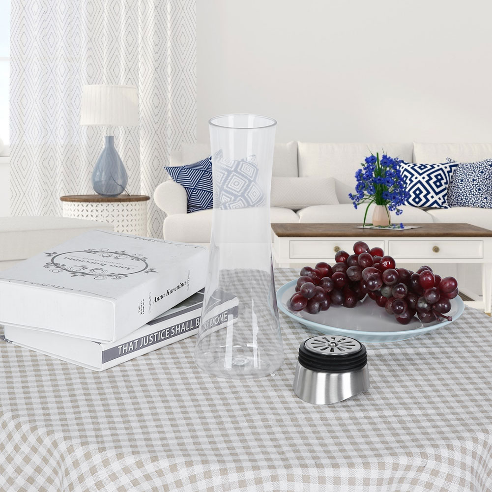 Ein Tisch mit einer Glasvase, Trauben, Büchern und einem Metallfilter. Hintergrund: Sofa, Vorhänge und eine Lampe.