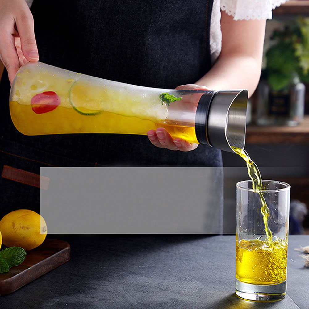 Eine Person gießt gelbe Flüssigkeit aus einem Krug in ein Glas. Zitronen und Minze liegen auf einem Holzbrett. Die Szene ist drinnen.