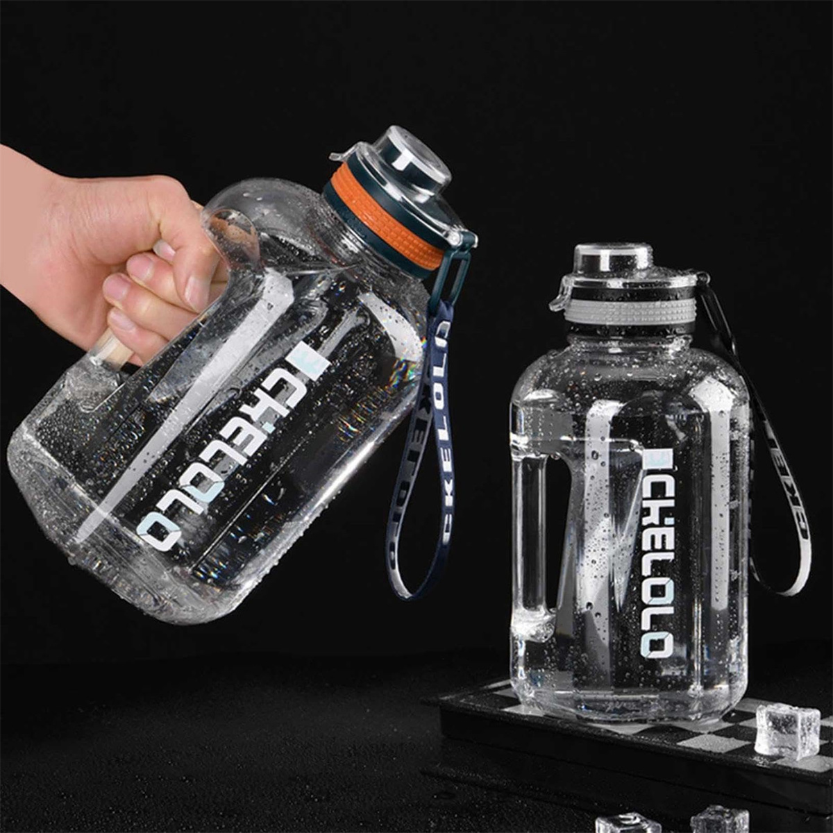 Zwei klare Wasserflaschen mit 'CHELOLO'-Text. Eine wird von einer Hand gehalten. Beide haben Wassertröpfchen. Eine steht auf karierter Oberfläche.