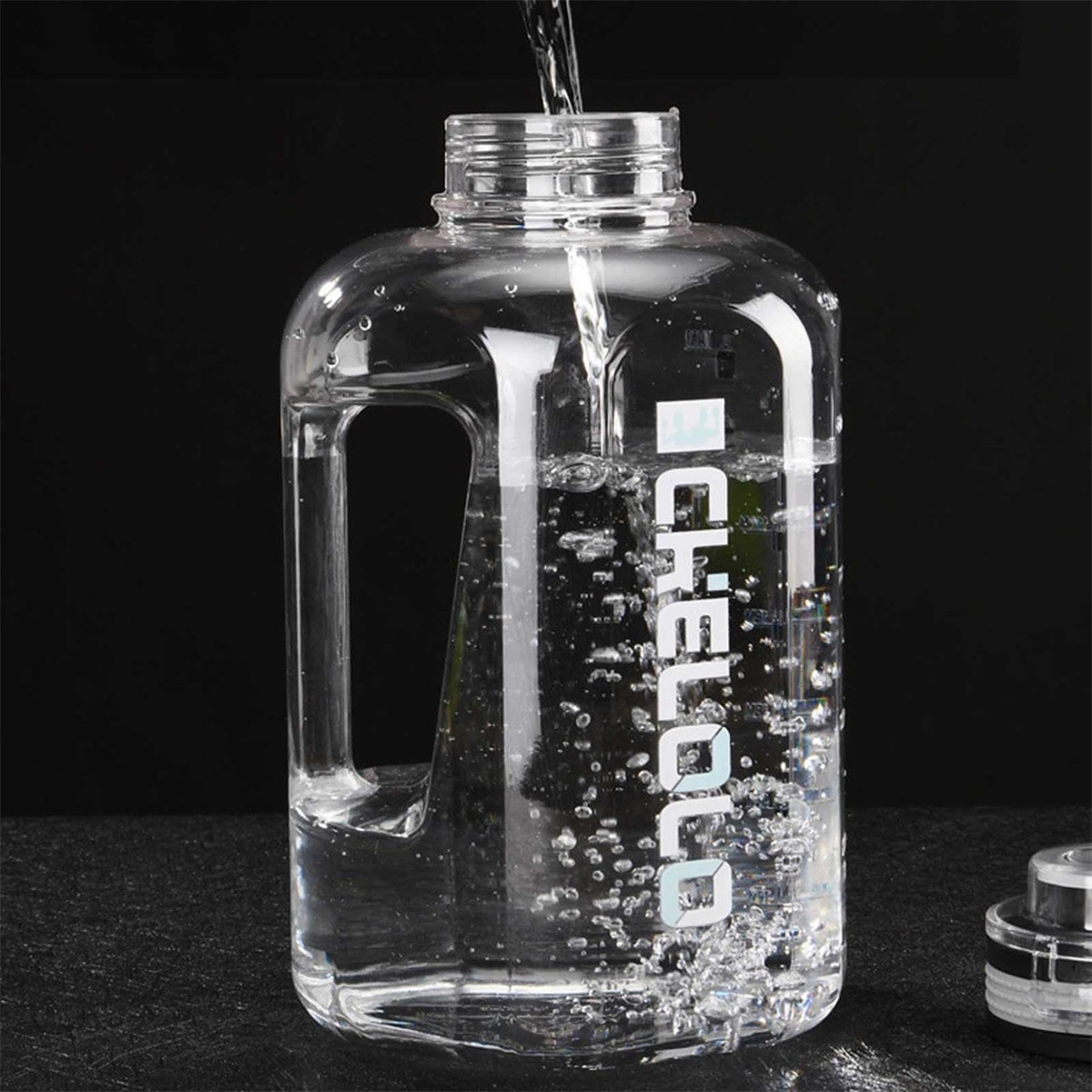 Eine klare Wasserflasche wird mit Wasser gefüllt. Wasser gießt von oben in die Flasche. Die Flasche hat einen Griff und weißen Text.