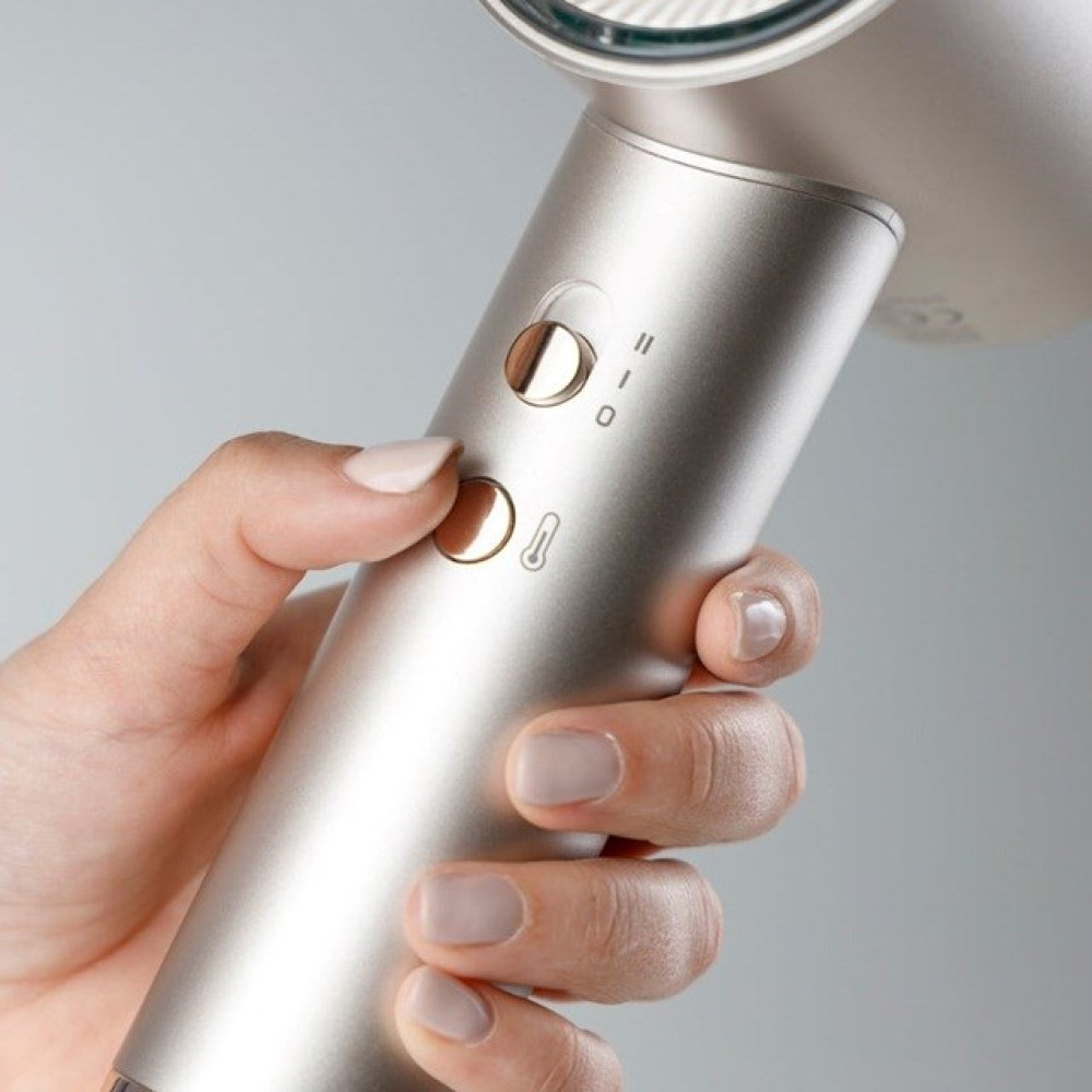 Ręka trzyma srebrną suszarkę do włosów. Ręka naciska przycisk. Tło jest jasnoszare.