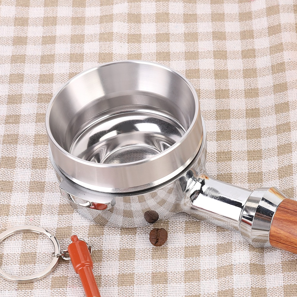 Ein verchromter Espressomaschinen-Siebträger mit Holzgriff, zwei Kaffeebohnen und einem kleinen roten Zubehörteil auf kariertem Stoff.