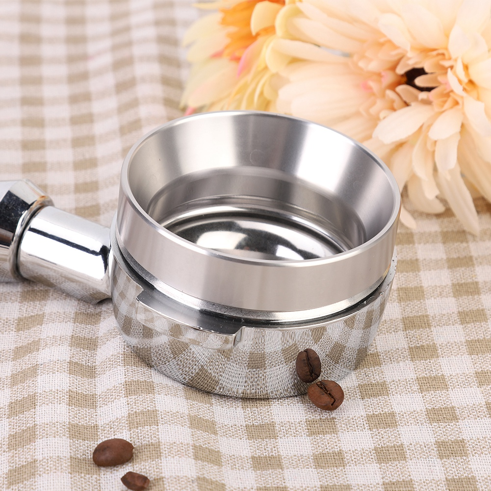 Ein verchromter Espressomaschinen-Siebträger liegt auf einem karierten Tuch, mit Kaffeebohnen in der Nähe und einer Blume im Hintergrund.