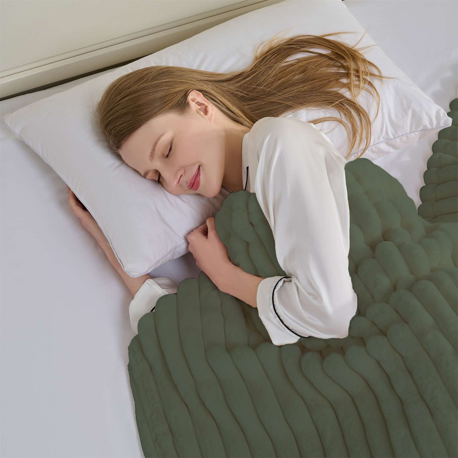 Frau schläft im Bett, bedeckt mit einer grünen Decke. Sie trägt einen weißen Pyjama und liegt auf einem weißen Kissen.