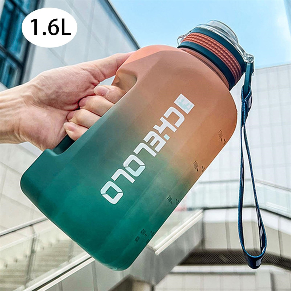Eine Hand hält eine 1,6-Liter-Wasserflasche. Sie ist grün und orange mit weißem Text. Sie hat einen blauen Riemen und einen durchsichtigen Deckel.