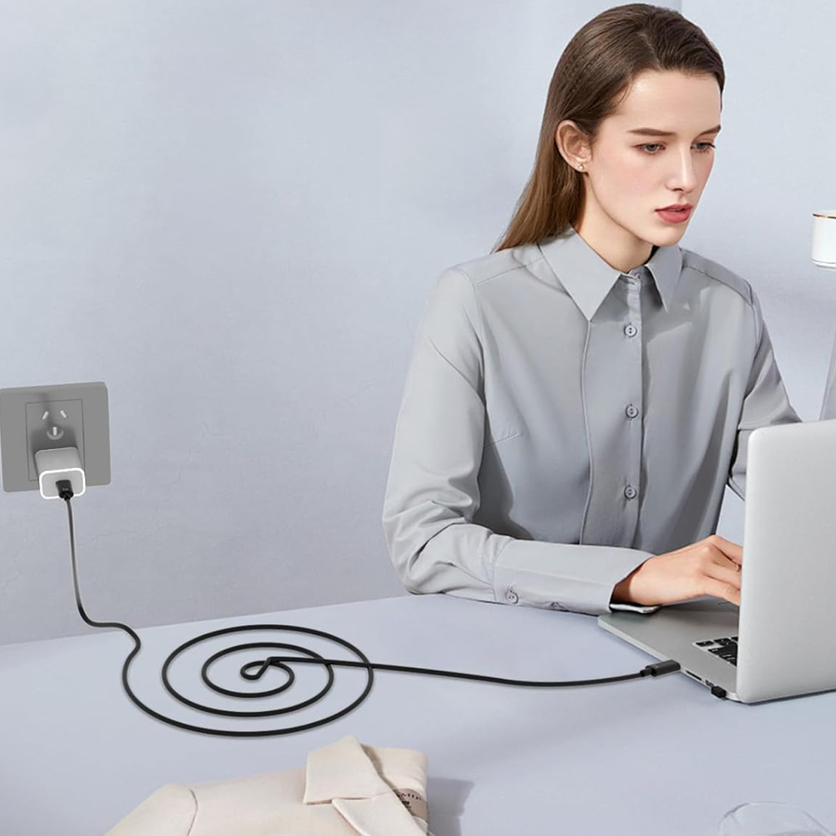 Eine Frau arbeitet mit einem Laptop, der an eine Steckdose angeschlossen ist. Ein schwarzes Kabel liegt auf dem Tisch.