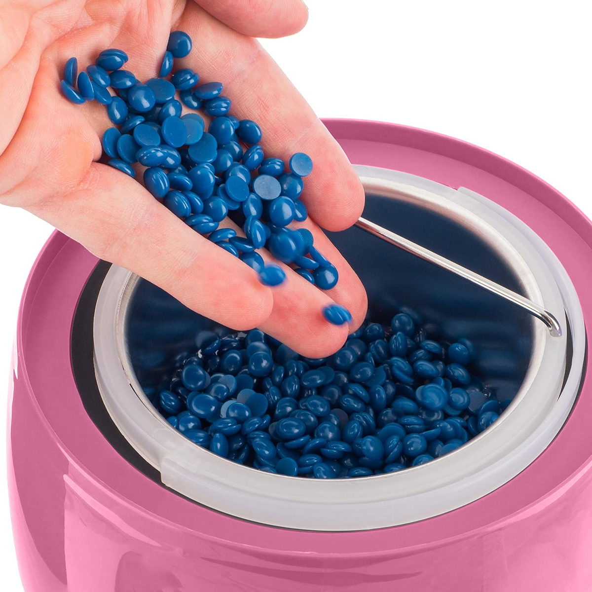 Eine Hand schüttet blaue Wachskügelchen in einen rosa Wachswärmer. Der Wärmer ist teilweise mit ähnlichen Kügelchen gefüllt.