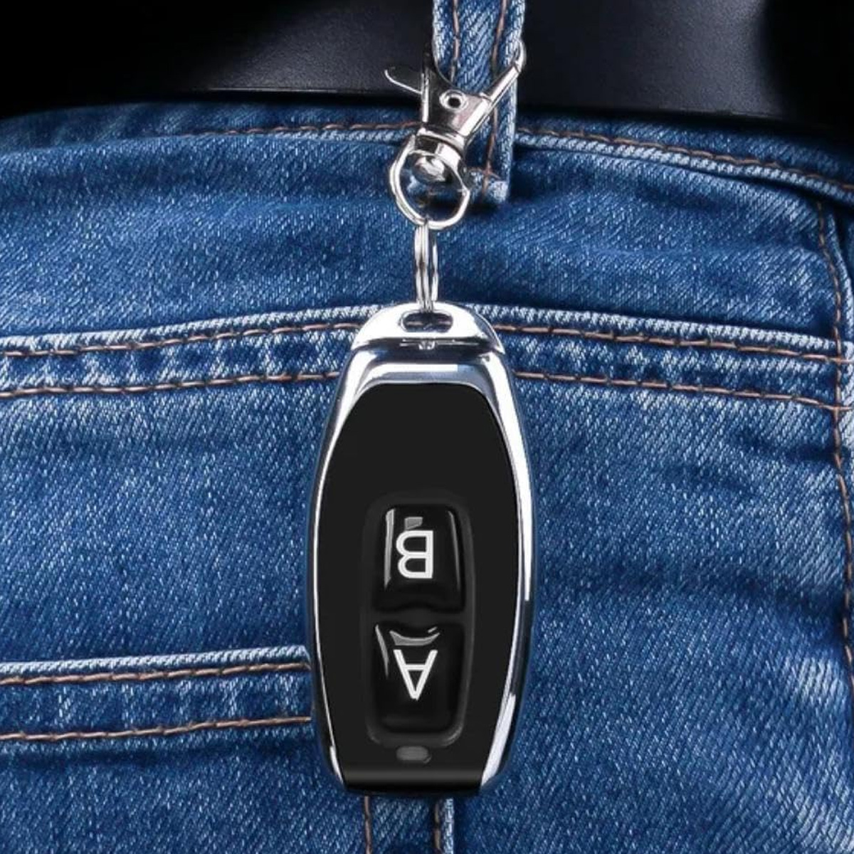 Ein schwarzer Schlüsselanhänger mit silberner Umrandung hängt an einer Jeans-Tasche. Zwei Knöpfe mit der Aufschrift A und B sind sichtbar.