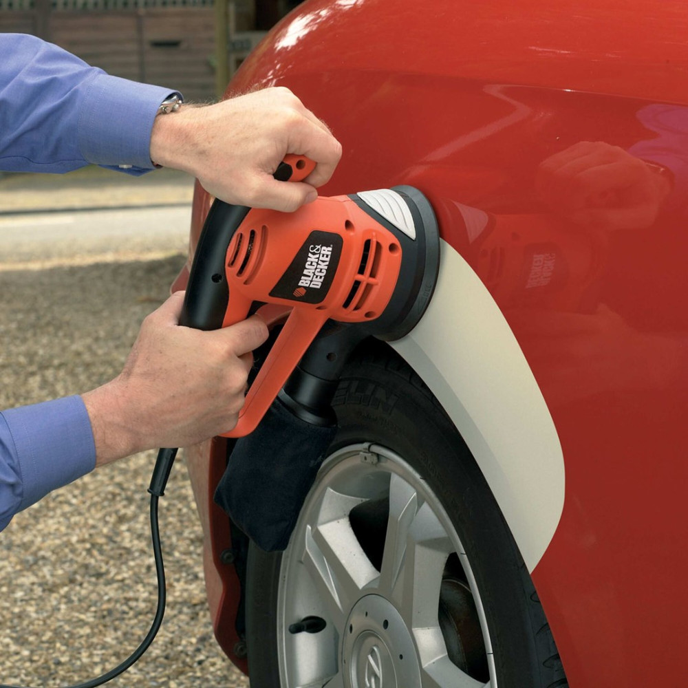 Osoba używa polerki Black & Decker na czerwonym samochodzie. Polerka jest pomarańczowo-czarna. Widoczne jest koło samochodu.