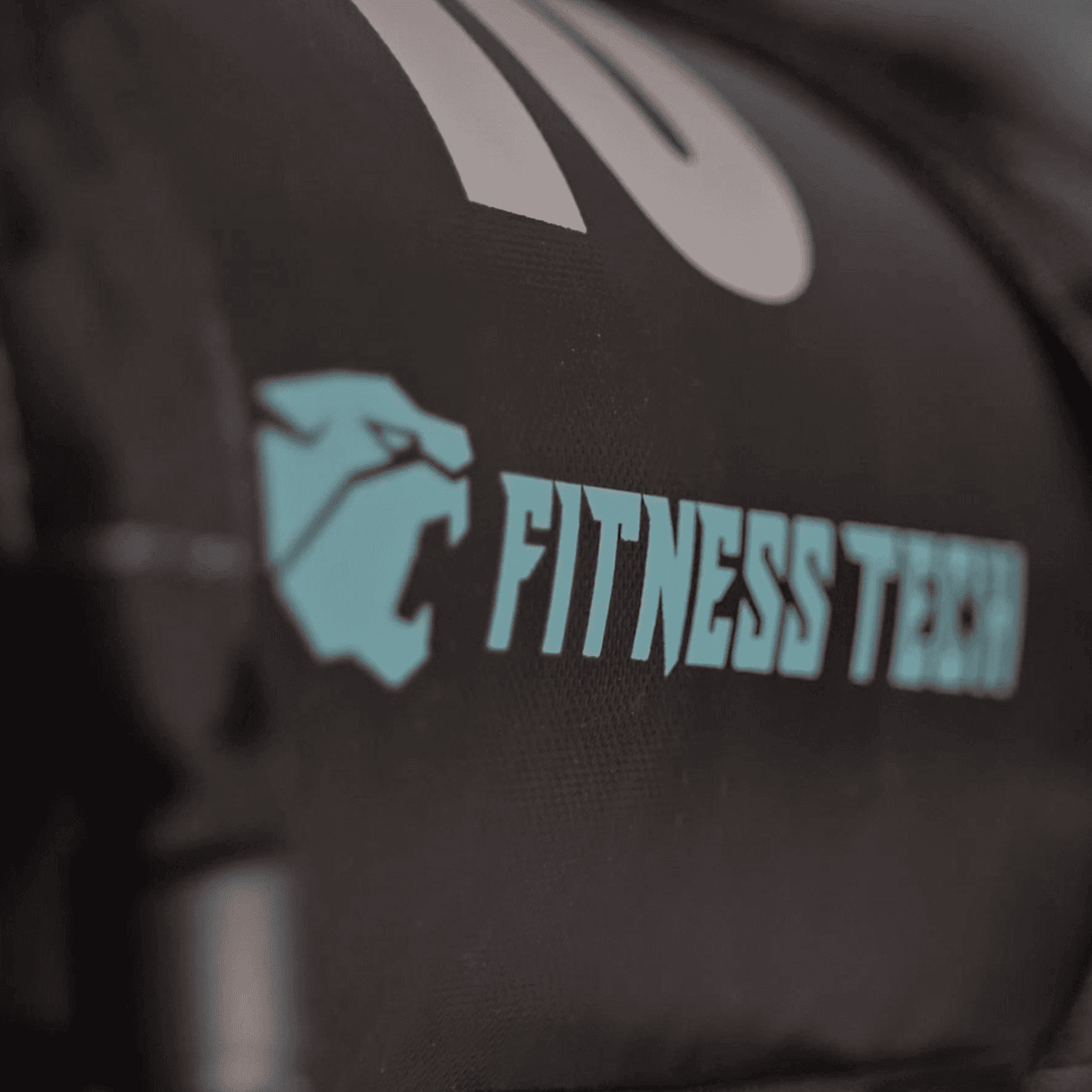 Primer plano de una bolsa negra con el logotipo 'Fitness Tech' en color turquesa. También es visible una cabeza de león estilizada.