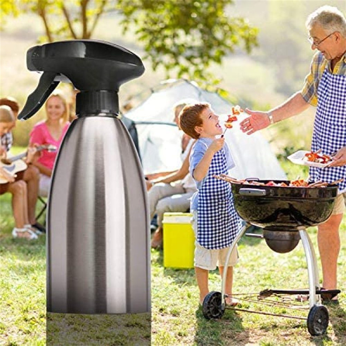 Ein Metallsprühgerät für Öl befindet sich im Vordergrund. Eine Familie genießt eine Grillparty. Ein Junge isst Essen von einem Spieß.