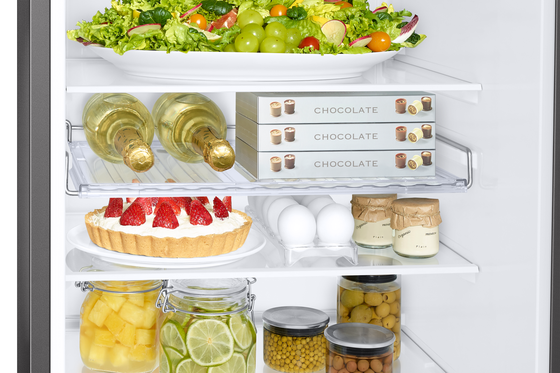 Kühlschrankinnenraum mit Salat, Champagner, Pralinenschachteln, Erdbeertorte, Eiern und Gläsern gefüllt.