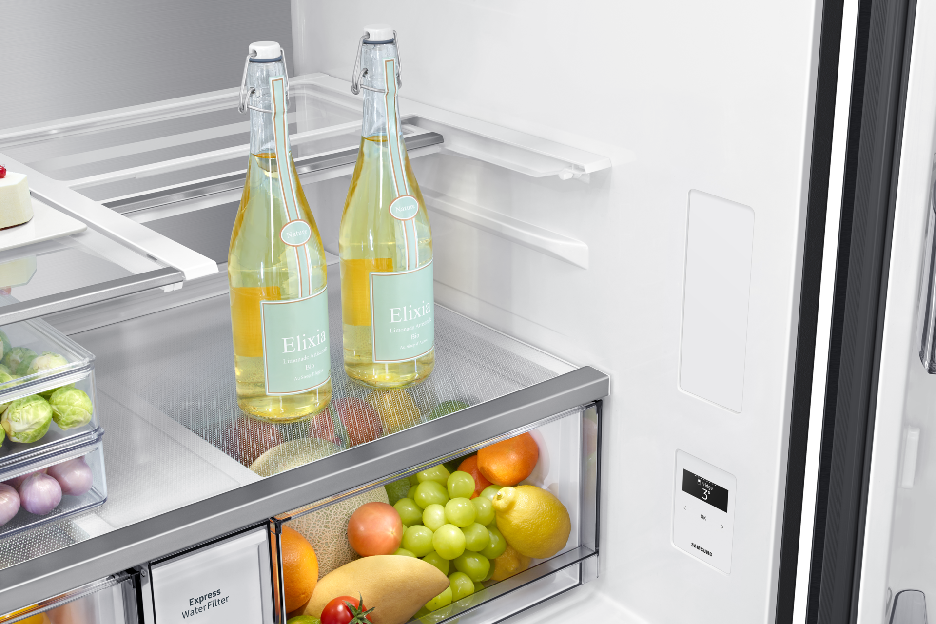 Im Kühlschrank befinden sich zwei Flaschen Elixia-Limonade, Obst und Gemüse in Schubladen. Ein Samsung-Bedienfeld ist ebenfalls sichtbar.