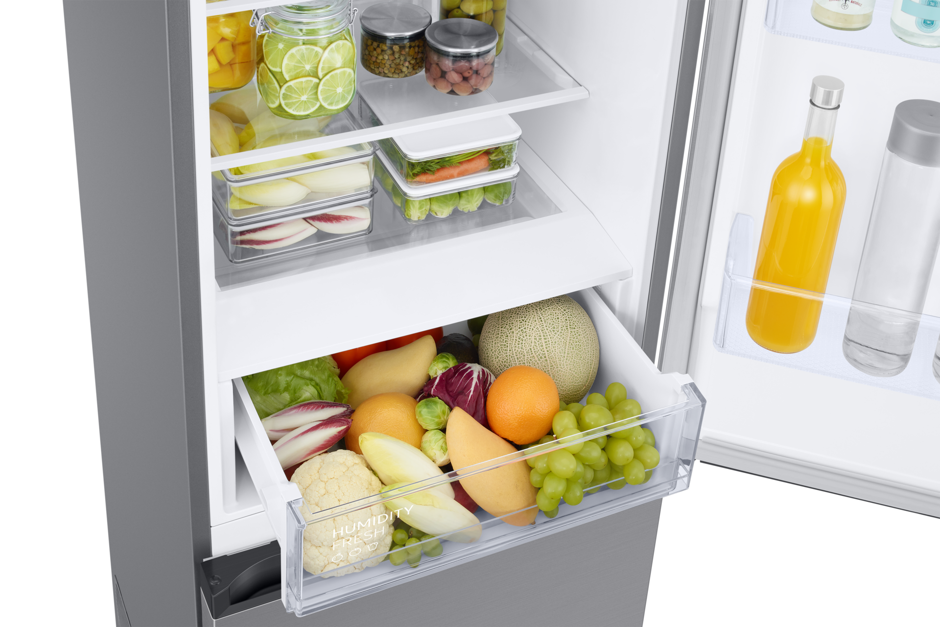 Offener Kühlschrank mit Obst und Gemüse in Schubladen und Regalen. Enthält Trauben, Orangen, Melone, Salat und Gläser mit Lebensmitteln.