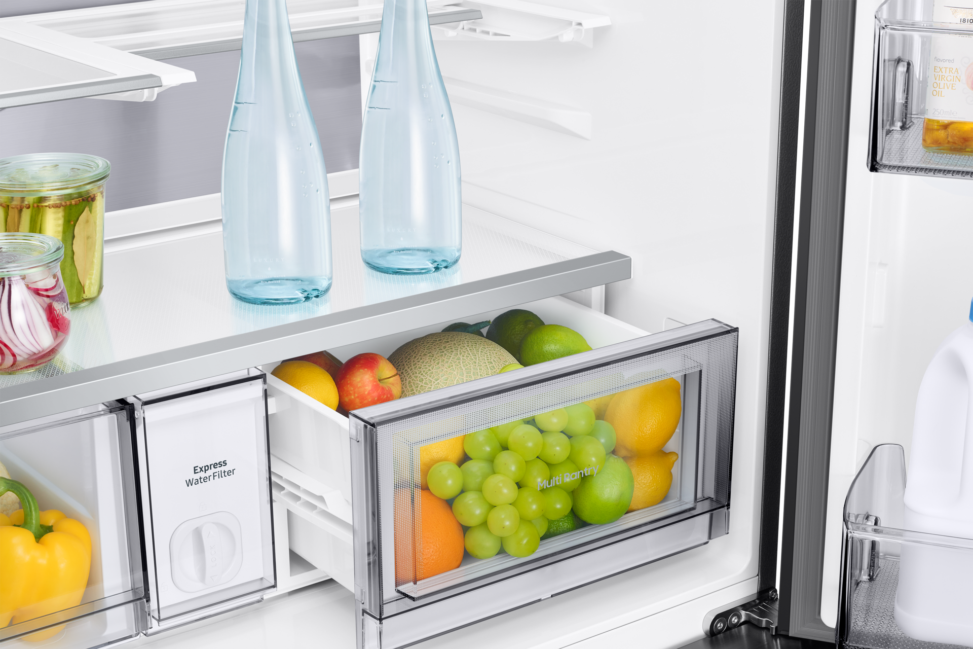 Otwarta lodówka z owocami i warzywami w szufladach, butelkami wody i słoikami na półkach. Zawiera jabłka, winogrona i cytryny.