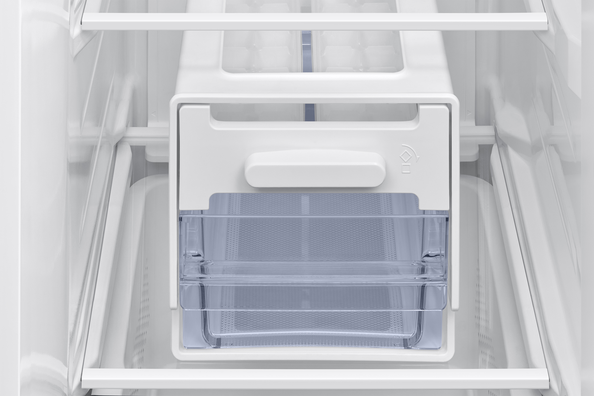 Wnętrze białej lodówki. Przezroczysta plastikowa szuflada pośrodku, nad nią biała kostkarka do lodu.